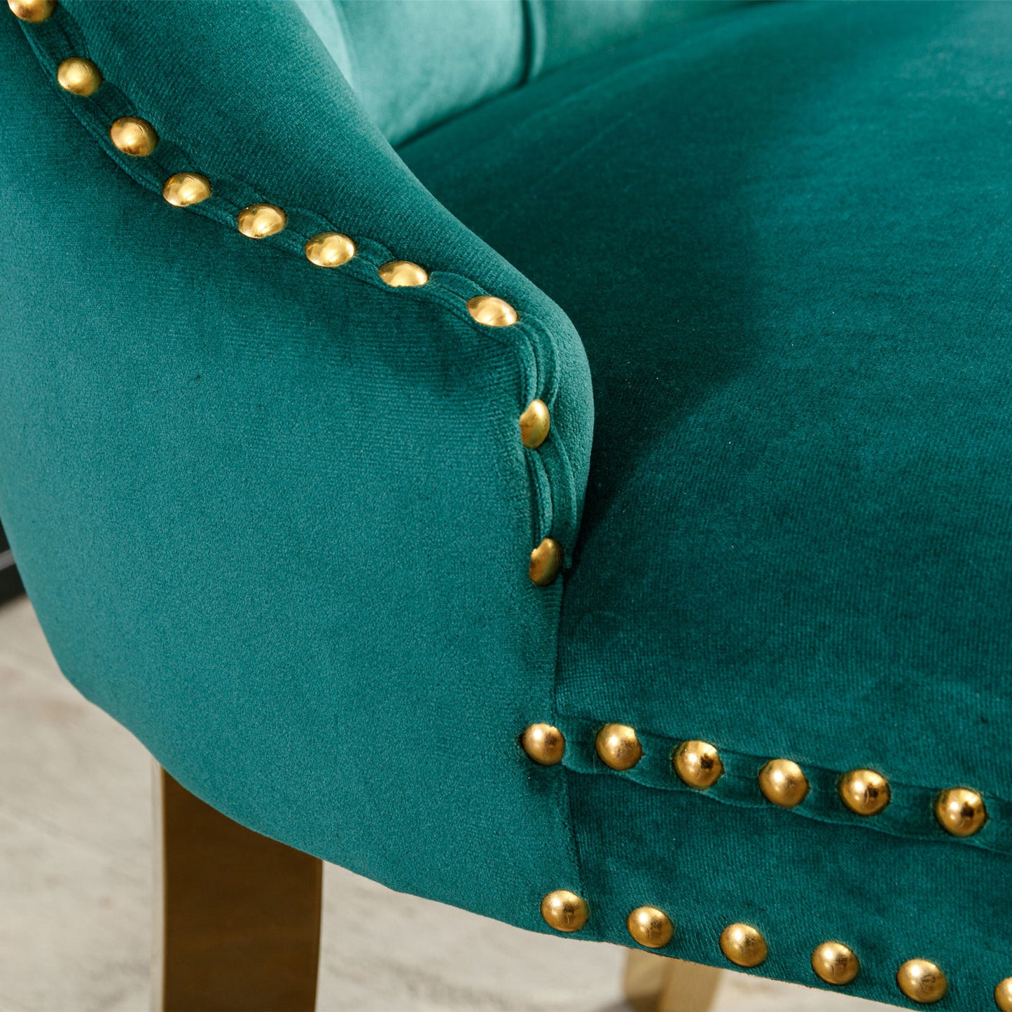Closeup of emerald green velvet chair arm with gold nailhead trim
