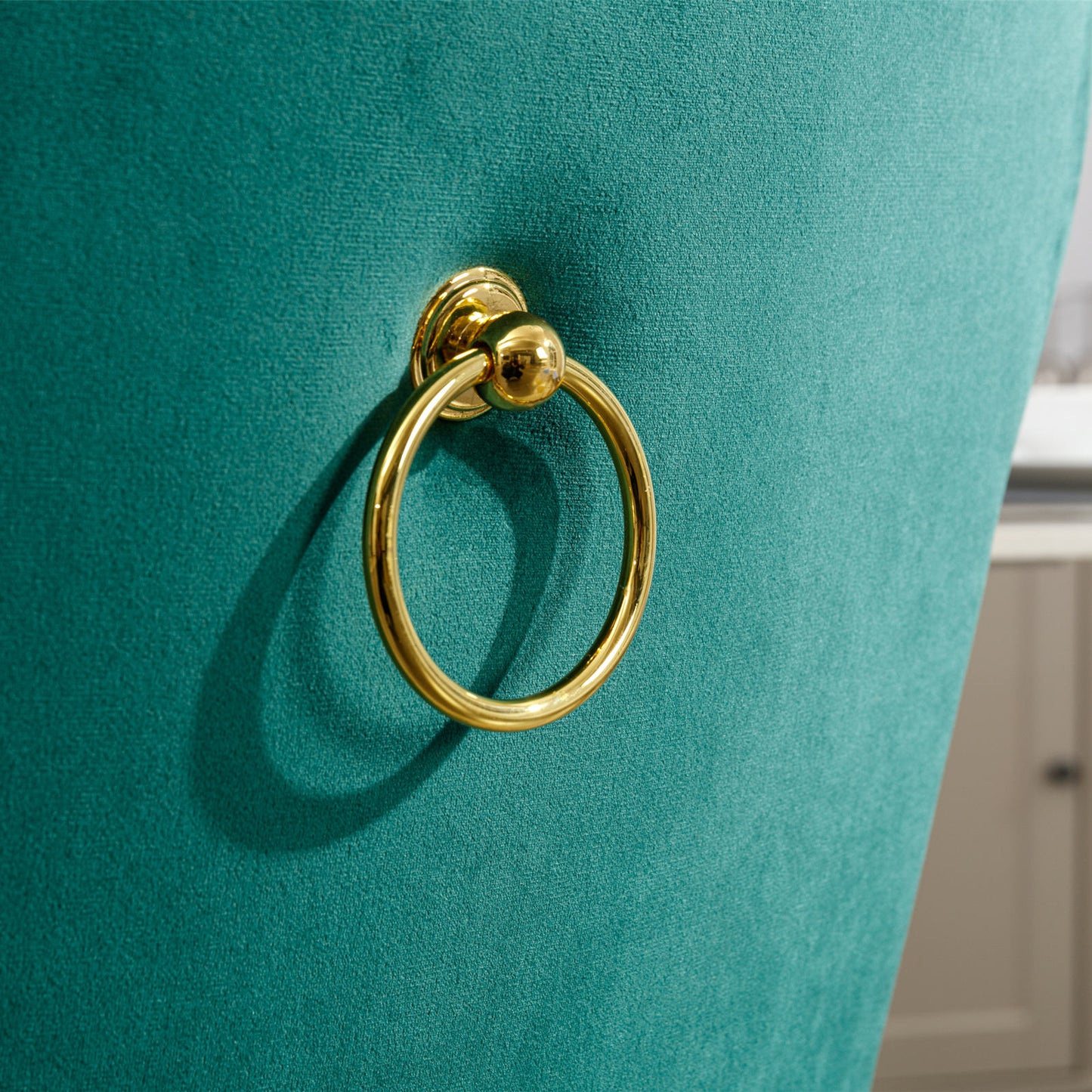Closeup of a teal velvet dining chair back with a gold ring pull accent