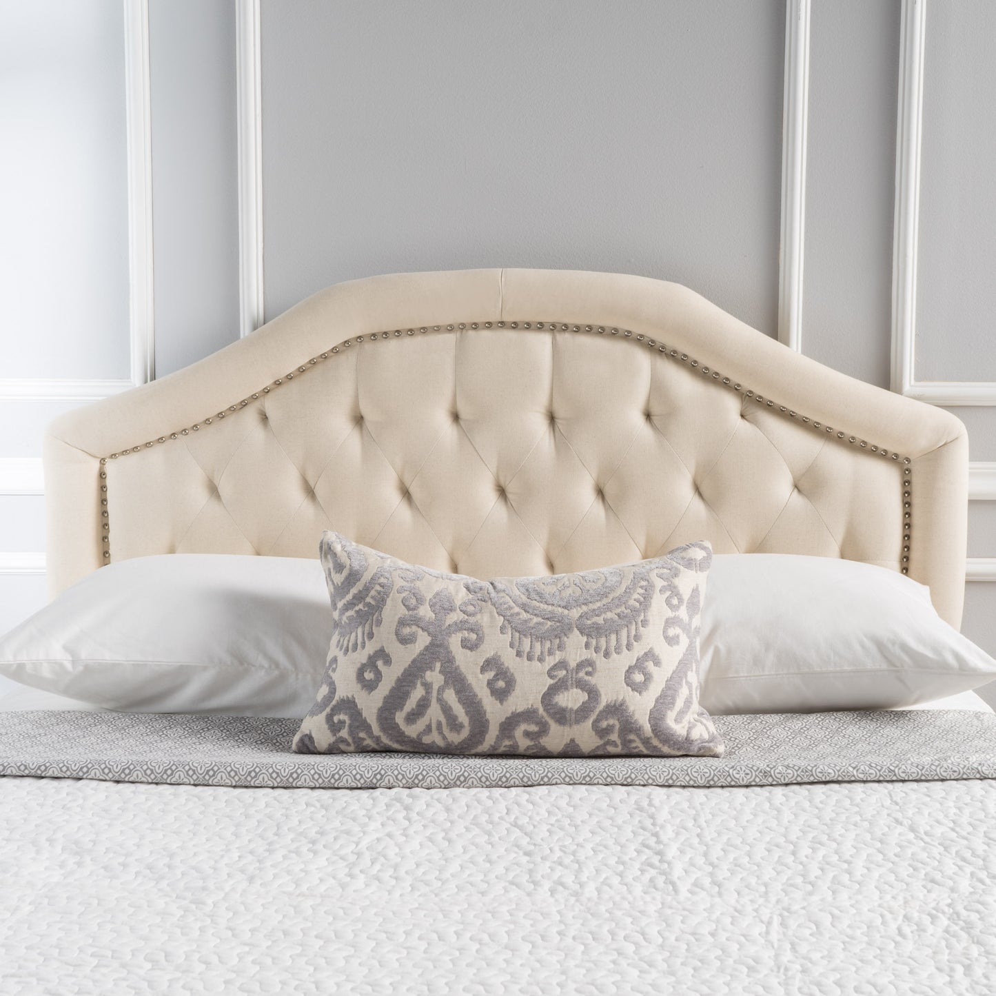 Tufted cream upholstered headboard with silver nailhead trim and a patterned lumbar pillow