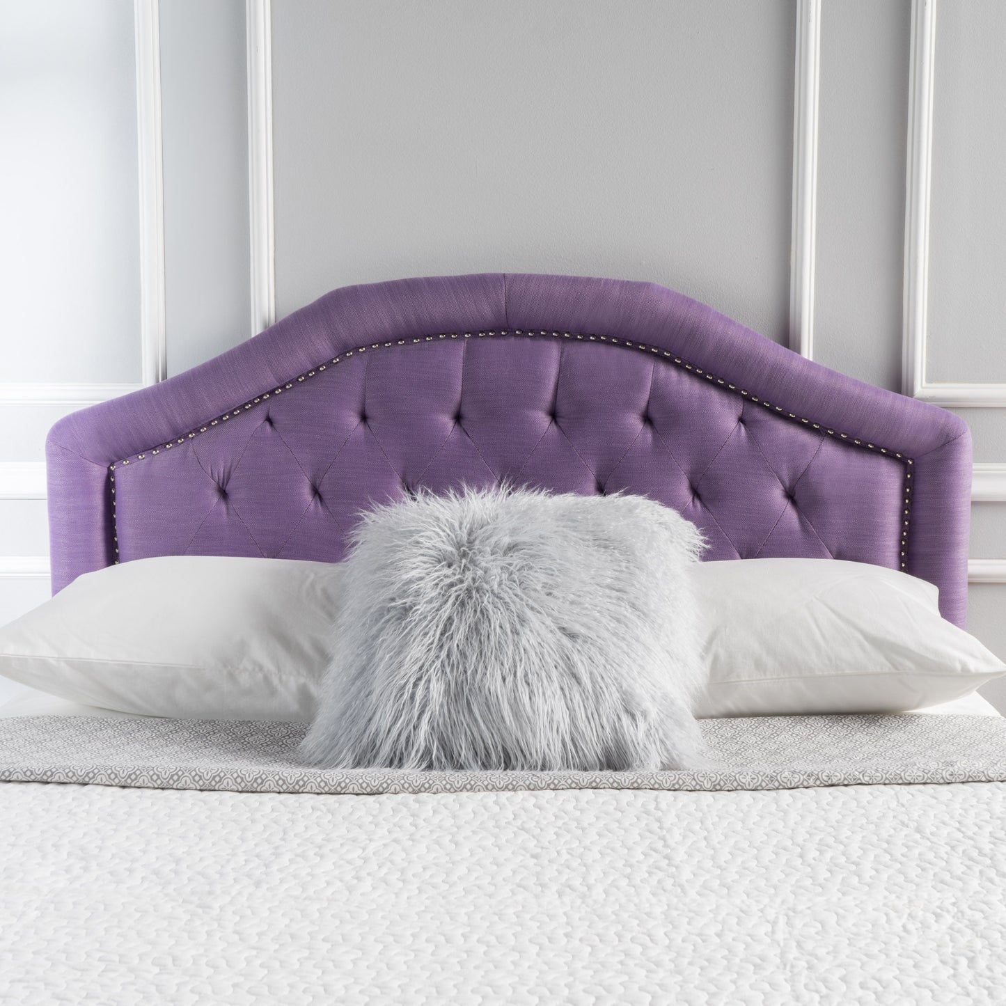 Tufted purple fabric headboard with nailhead trim on a bed with white pillows