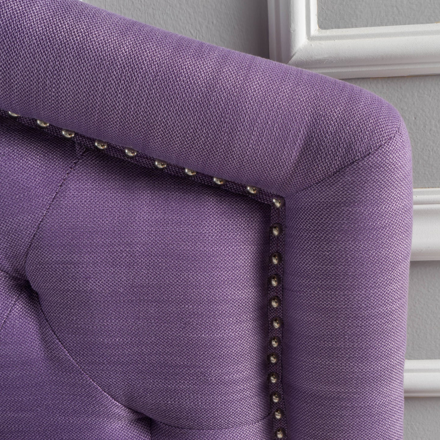 Closeup of tufted purple upholstered headboard with silver nailhead trim