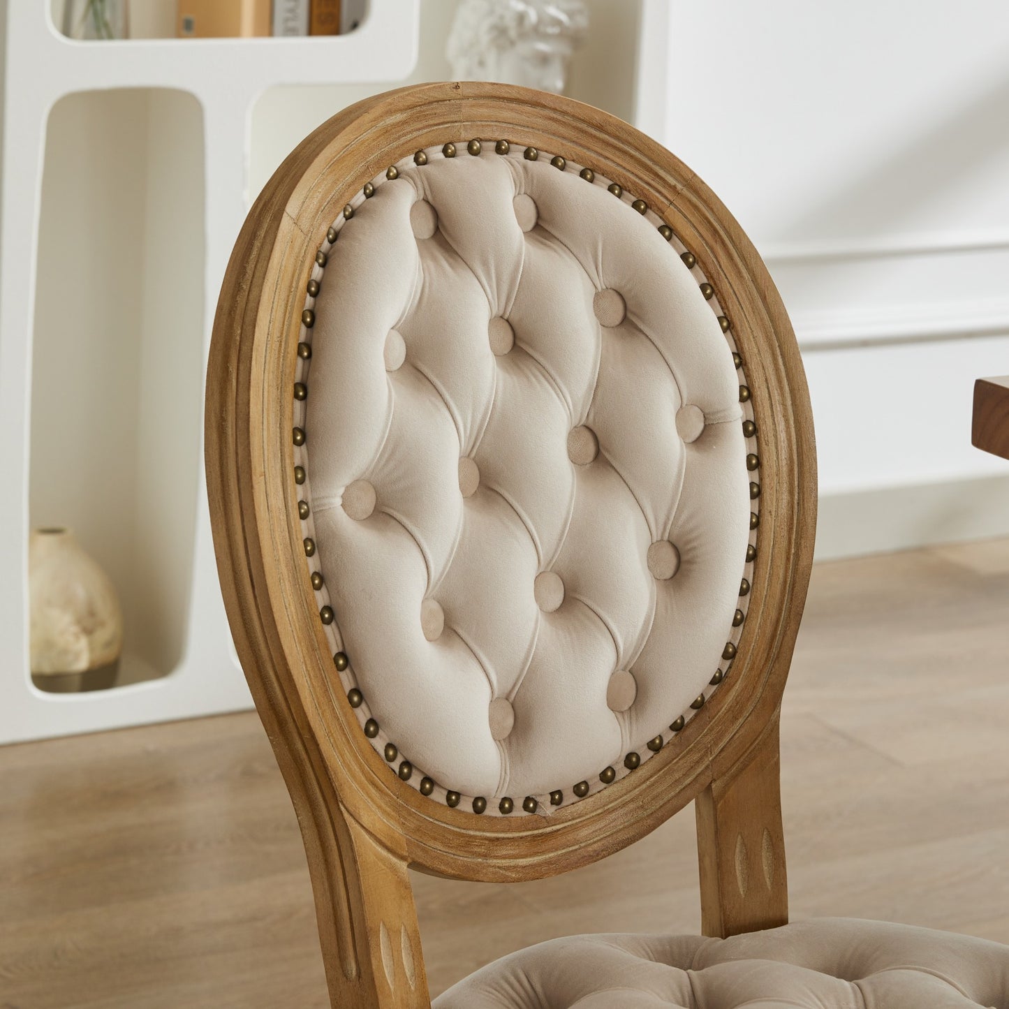 Tufted beige velvet dining chair with distressed wood frame and brass nailhead trim