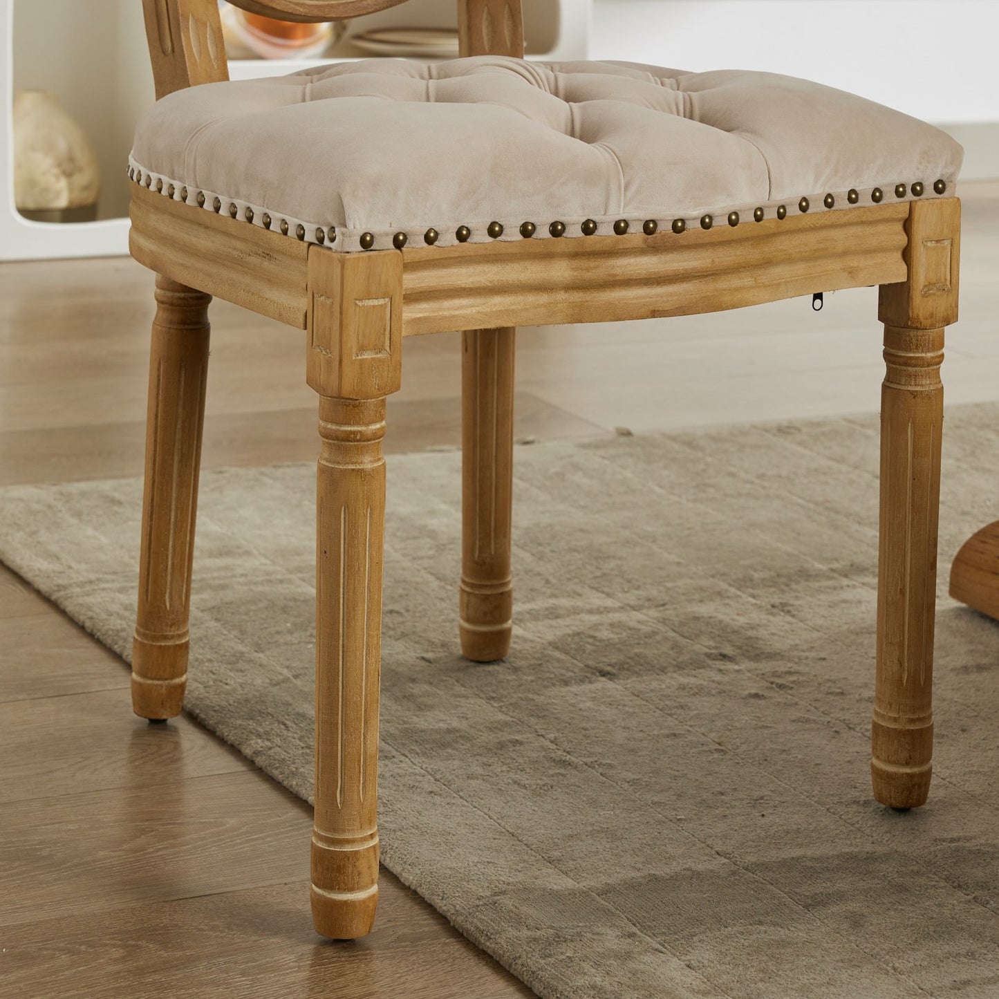 Tufted beige velvet dining chair with antique brass nailhead trim and carved wooden legs