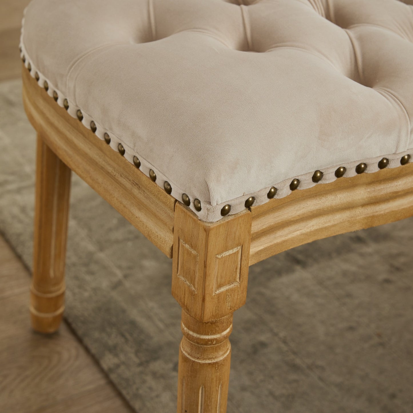 Beige velvet upholstered stool with tufted seat and brass nailhead trim