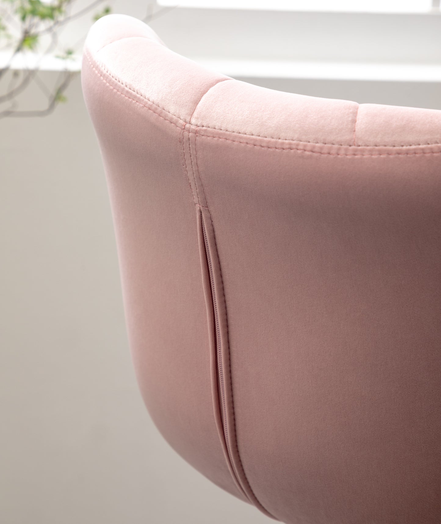 Closeup of a blush pink velvet accent chair back with tufted detailing and a subtle zipper closure