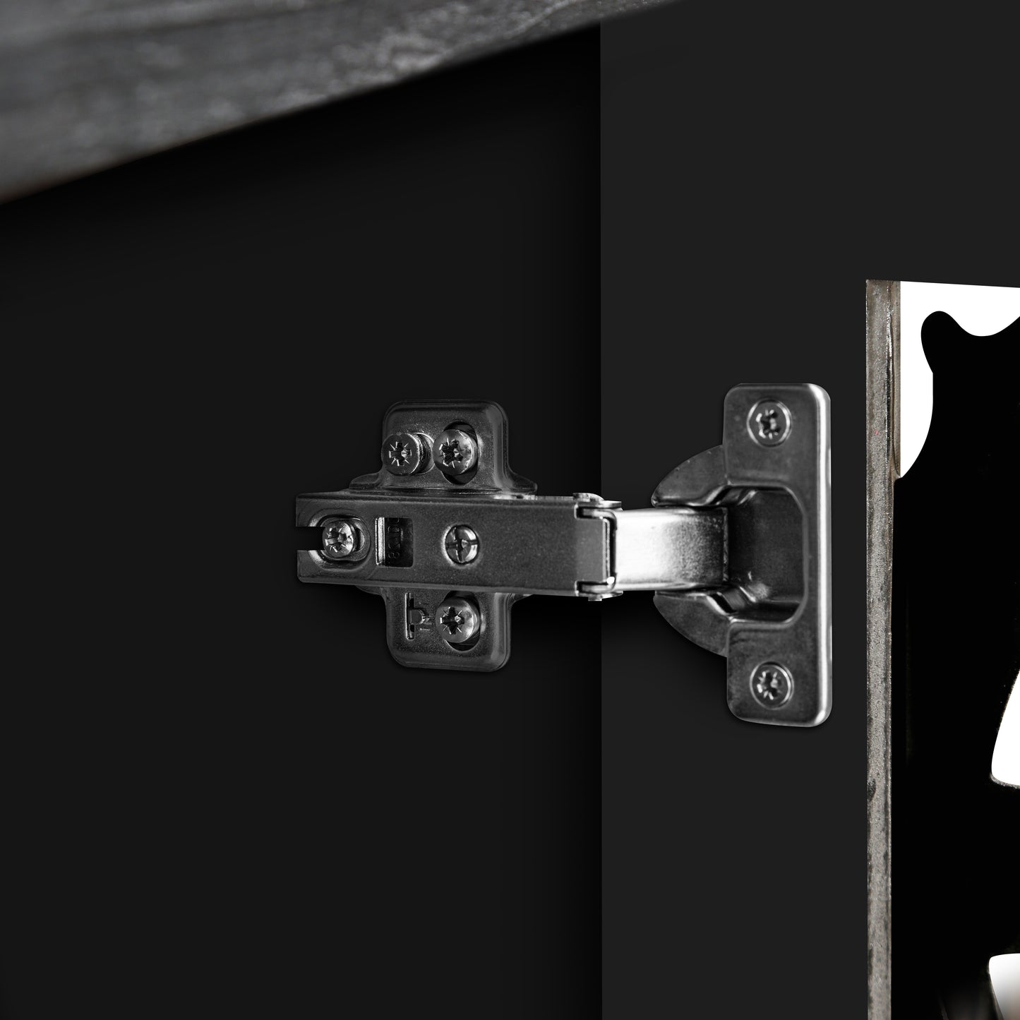 Closeup of a brushed nickel cabinet hinge attached to black cabinetry