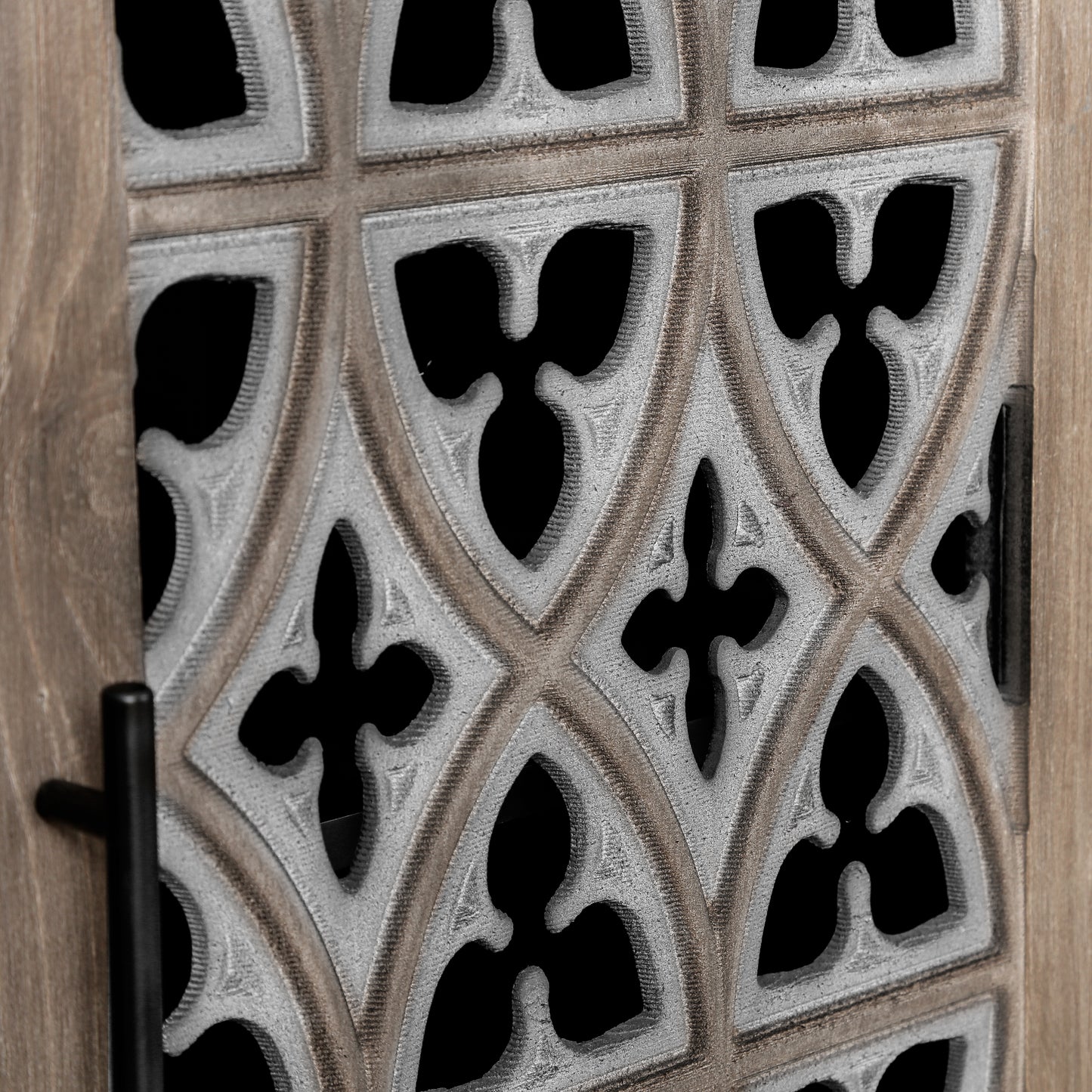 Closeup of antique wood cabinet door with decorative gothic fretwork detail and black handle