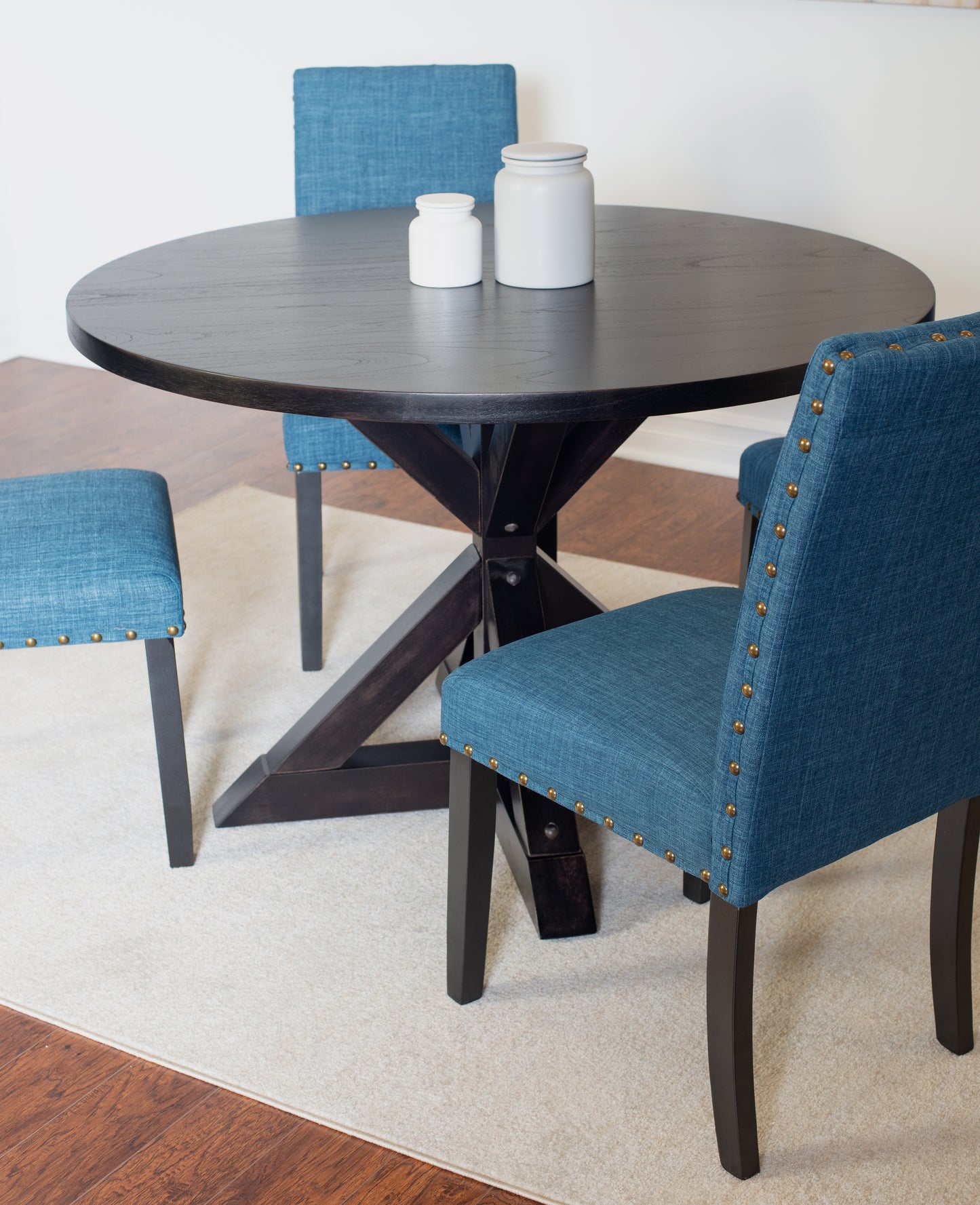 Round dark wood dining table with pedestal base and teal upholstered chairs
