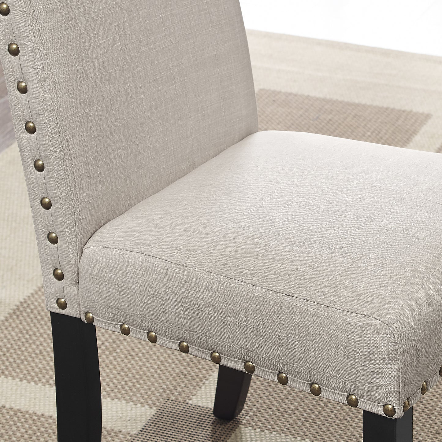 Closeup of a beige linen upholstered dining chair with brass nailhead trim