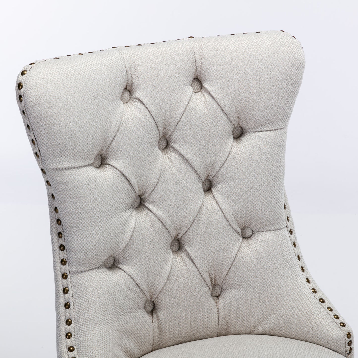 Closeup of a beige tufted upholstered armchair back with brass nailhead trim