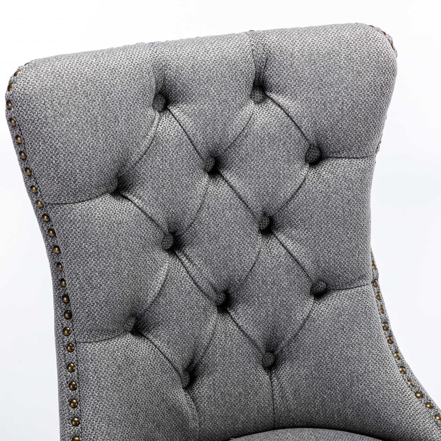 Closeup of tufted grey fabric dining chair back with brass nailhead trim