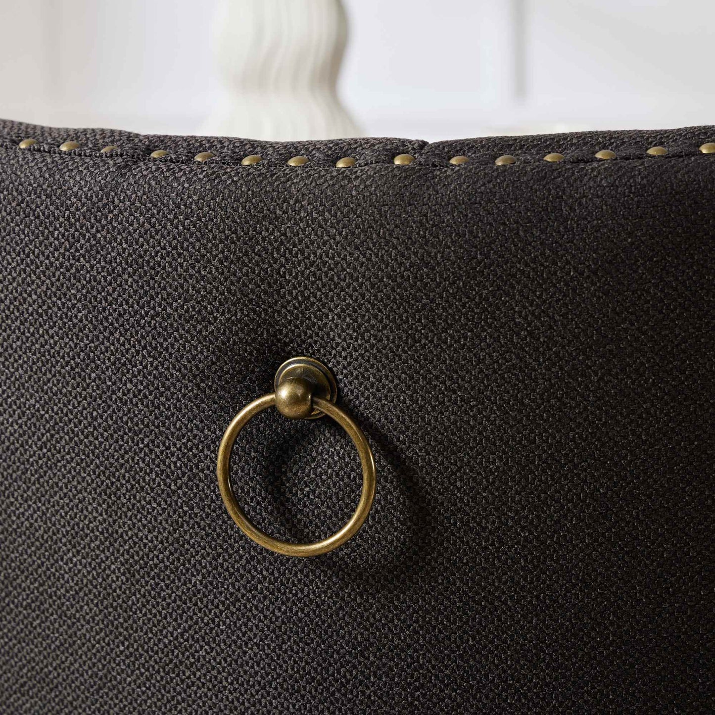 Dark grey upholstered chair back with brass ring pull and nailhead trim