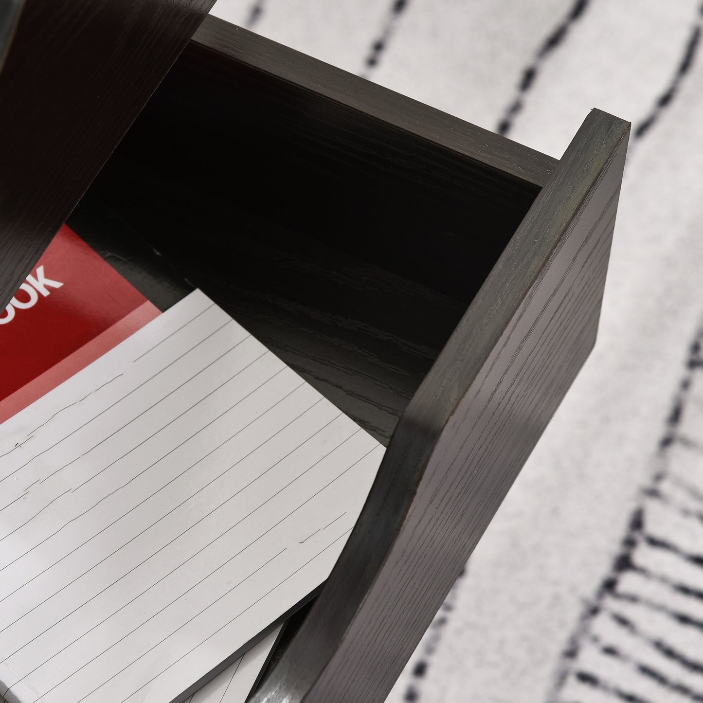Dark wood desk drawer with a red notebook and lined paper inside