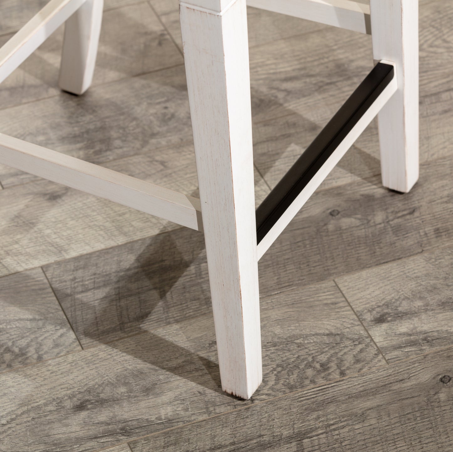 White distressed wood bar stool leg detail with black footrest