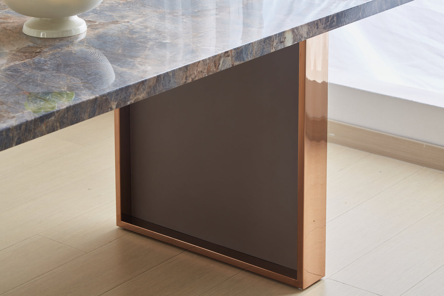 Polished marble tabletop with a rose gold metal leg on hardwood floor
