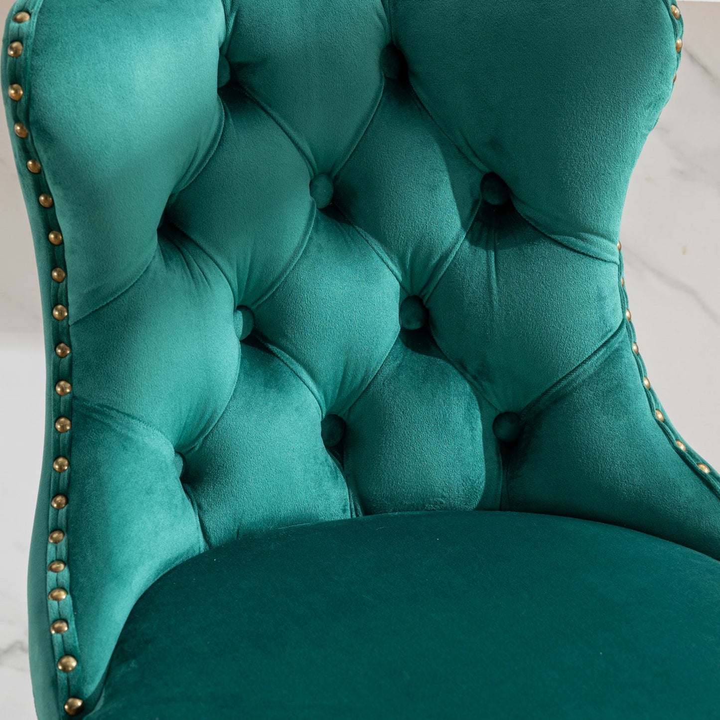 Deep emerald velvet dining chair with button tufting and gold nailhead trim