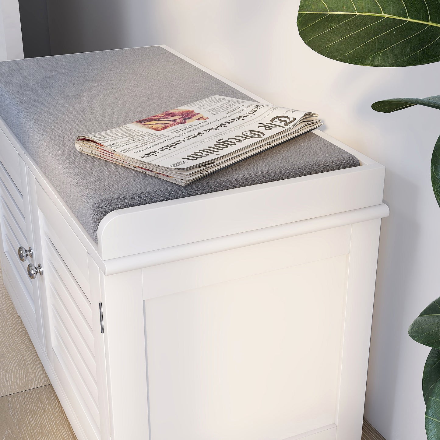 White shoe storage bench with grey upholstered seat and newspaper