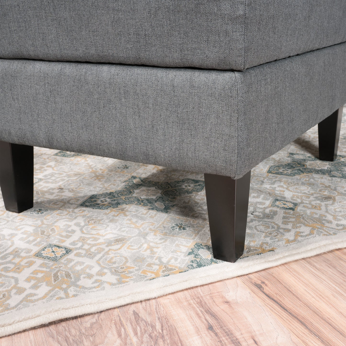 Gray upholstered ottoman corner with dark wood legs on patterned rug