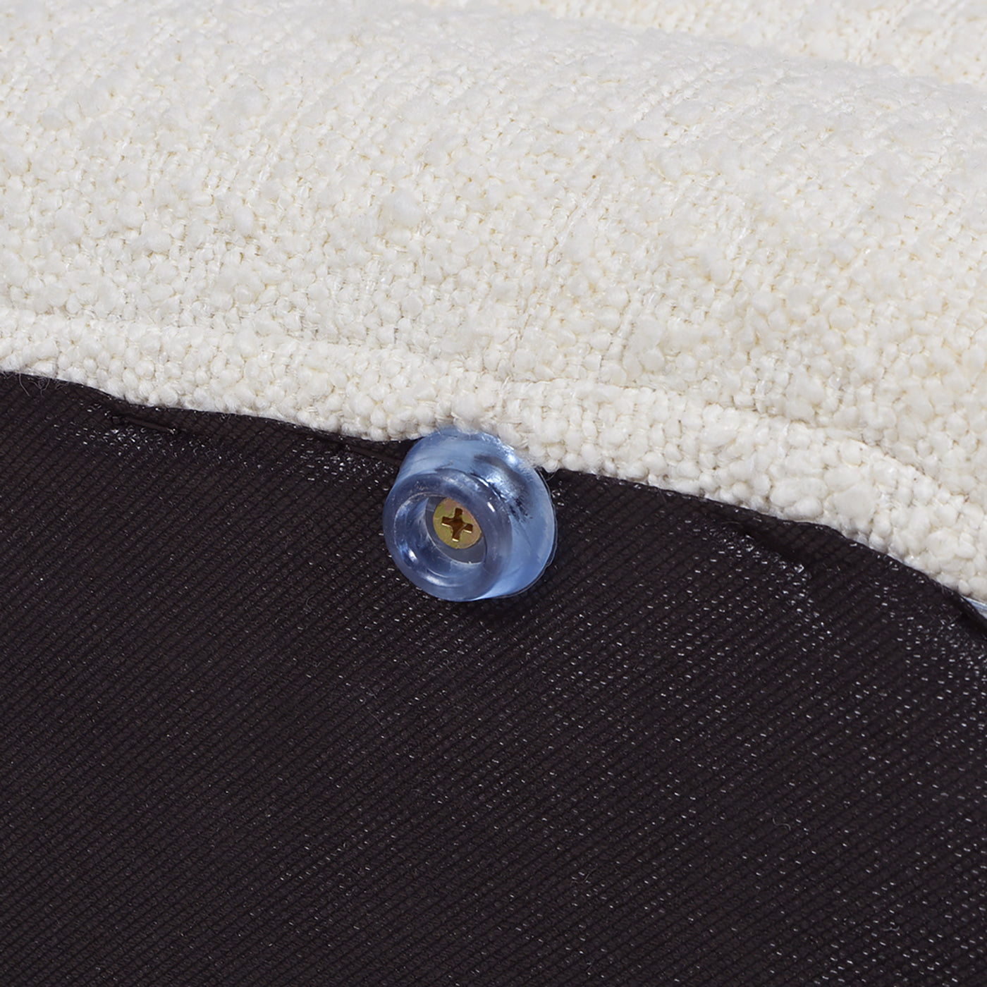 Closeup of a clear plastic furniture leg protector with a gold screw on a textured cream fabric ottoman
