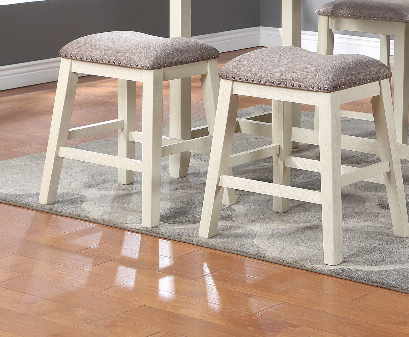Cream wooden counter stools with textured gray upholstered seats and brass tack trim