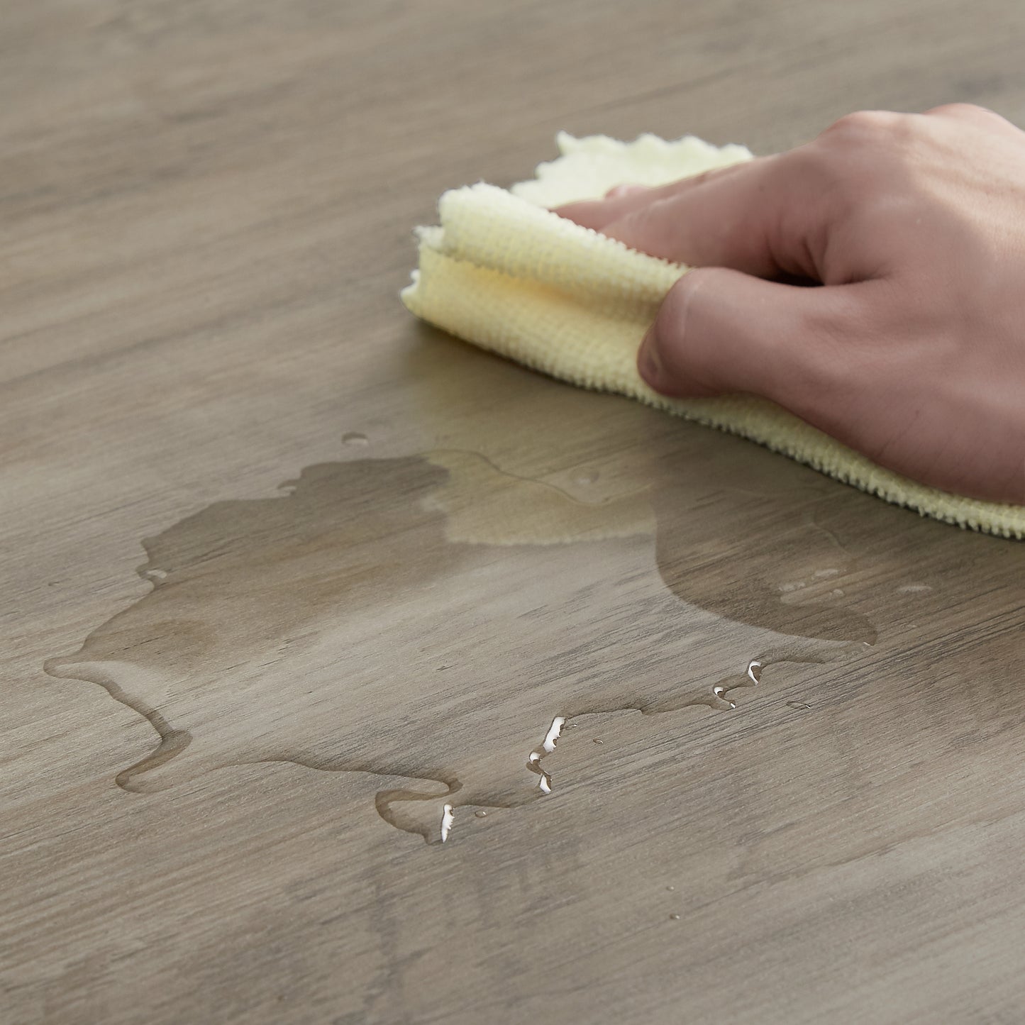 Yellow microfiber cloth wiping up water spills on woodlook laminate flooring