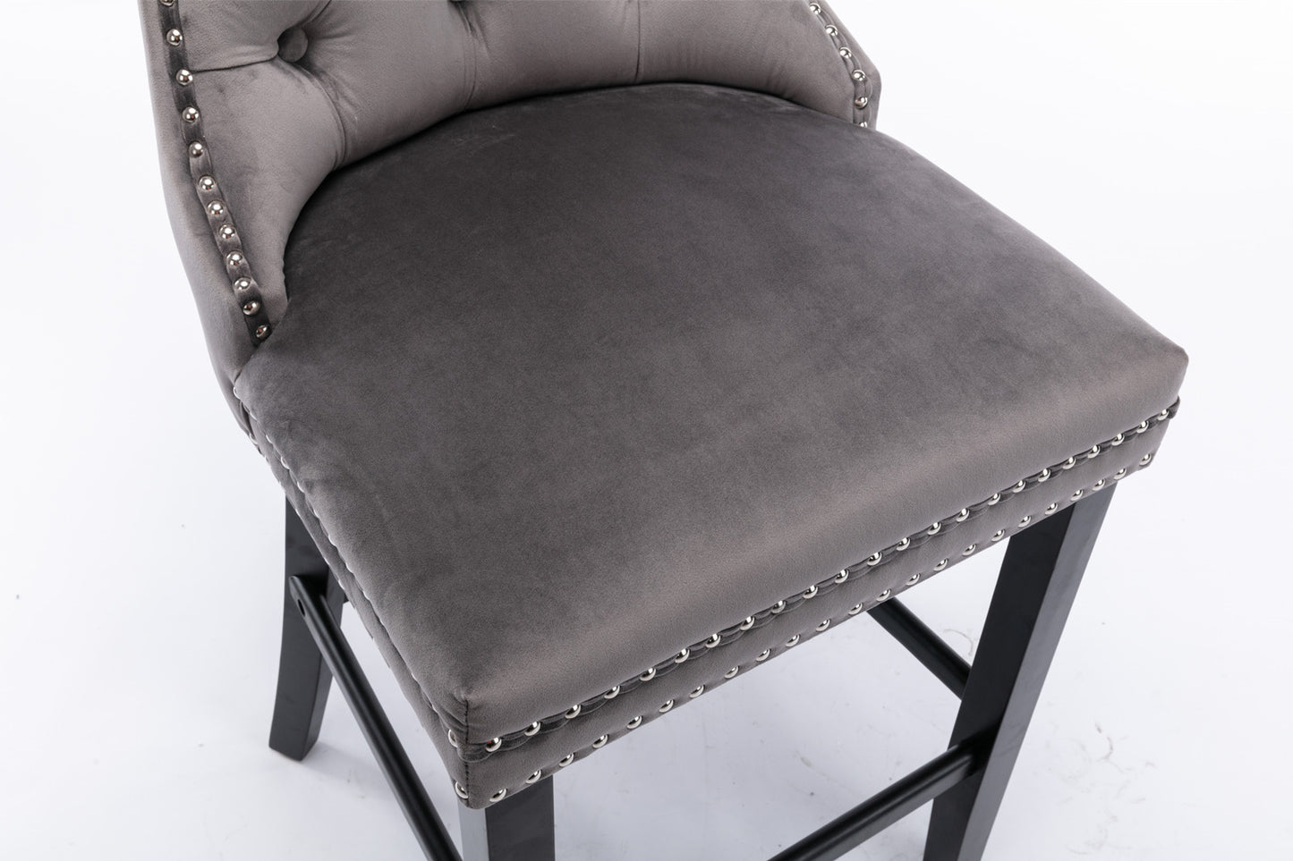 Closeup of tufted grey velvet bar stool with silver nailhead trim and dark wood legs