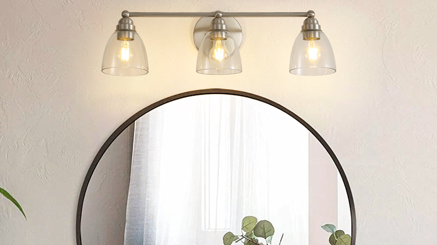 Brushed nickel vanity light with three clear glass shades above a darkframed round mirror