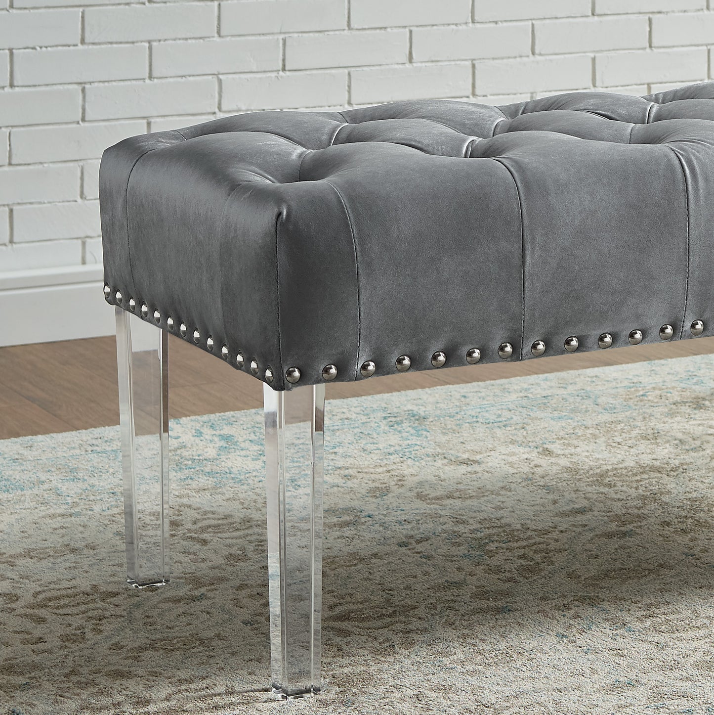 Tufted grey leather ottoman with silver nailhead trim and clear acrylic legs