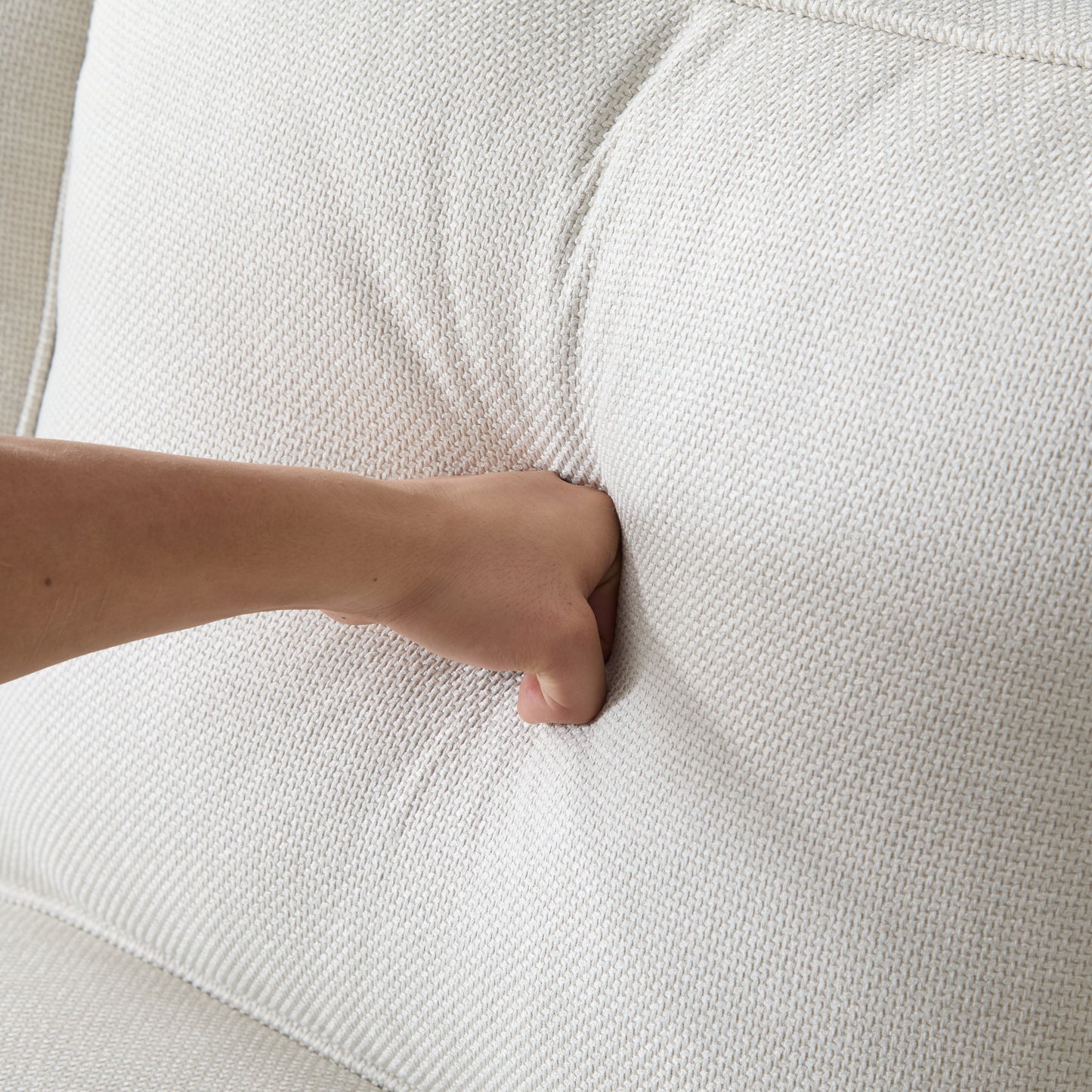 Hand pressing into a soft textured beige woven fabric cushion highlighting plush comfort