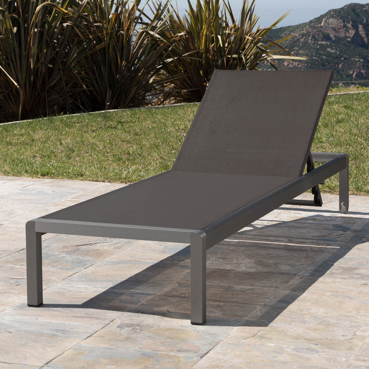 Charcoal grey outdoor chaise lounge with adjustable backrest on stone patio