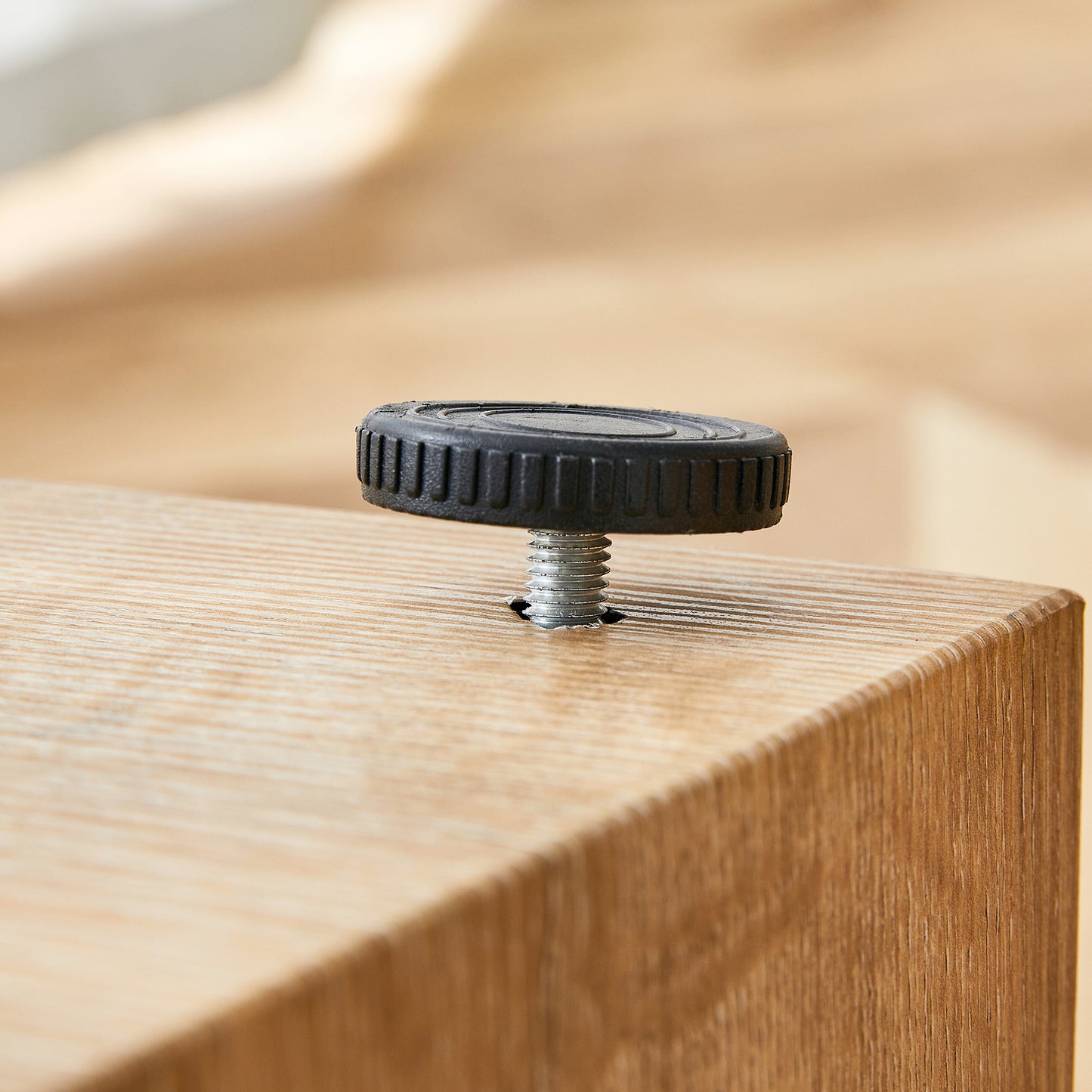 Black adjustable leveling foot with threaded bolt screwed into a wooden surface