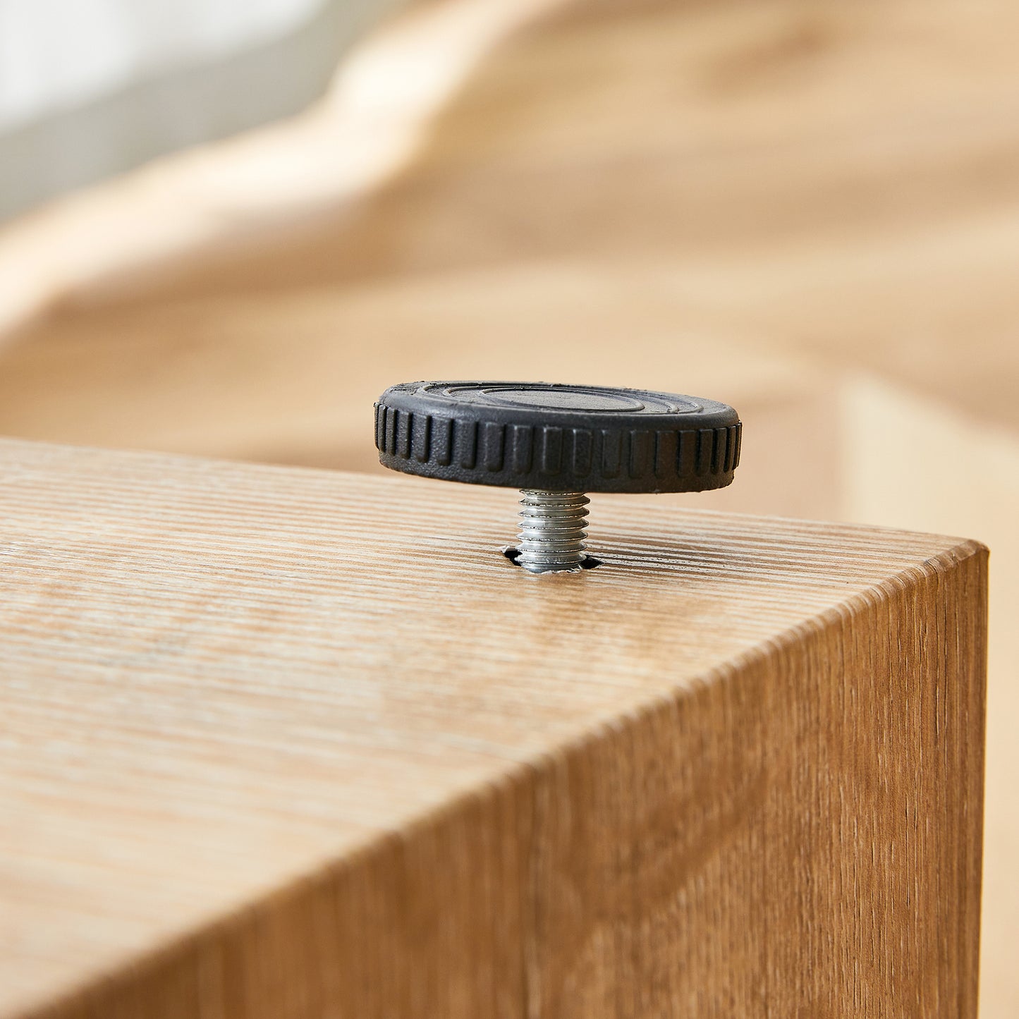 Black plastic adjustable furniture foot with metal screw thread on wood surface