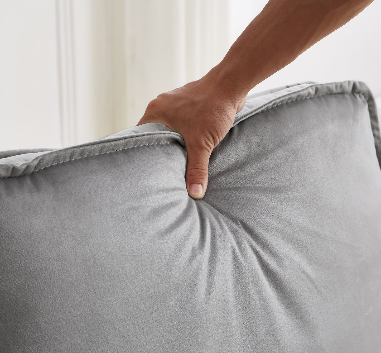 Closeup of a hand pressing into a plush grey velvet cushion