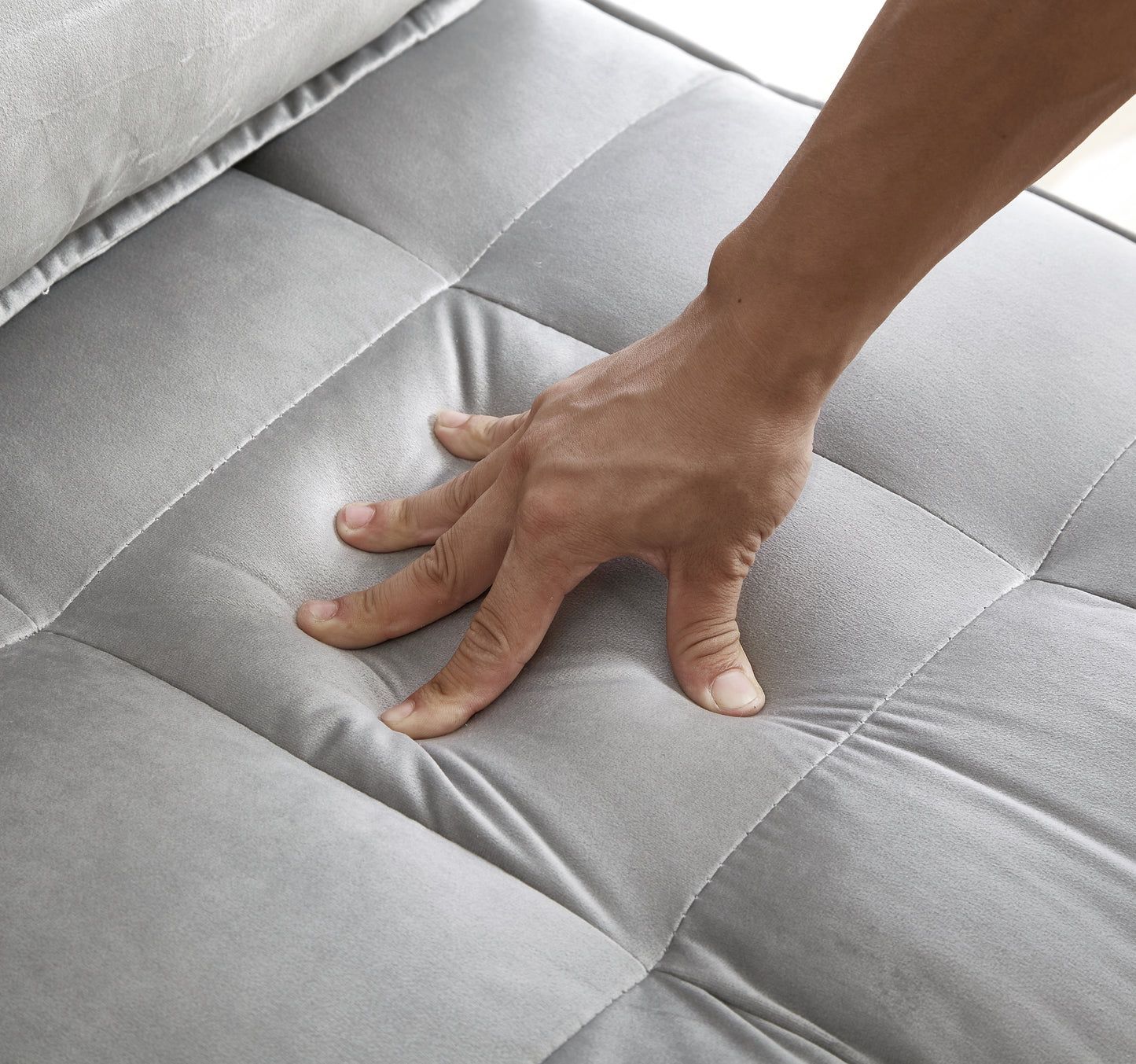 Closeup of a hand pressing into a plush grey velvet sofa cushion showcasing comfort