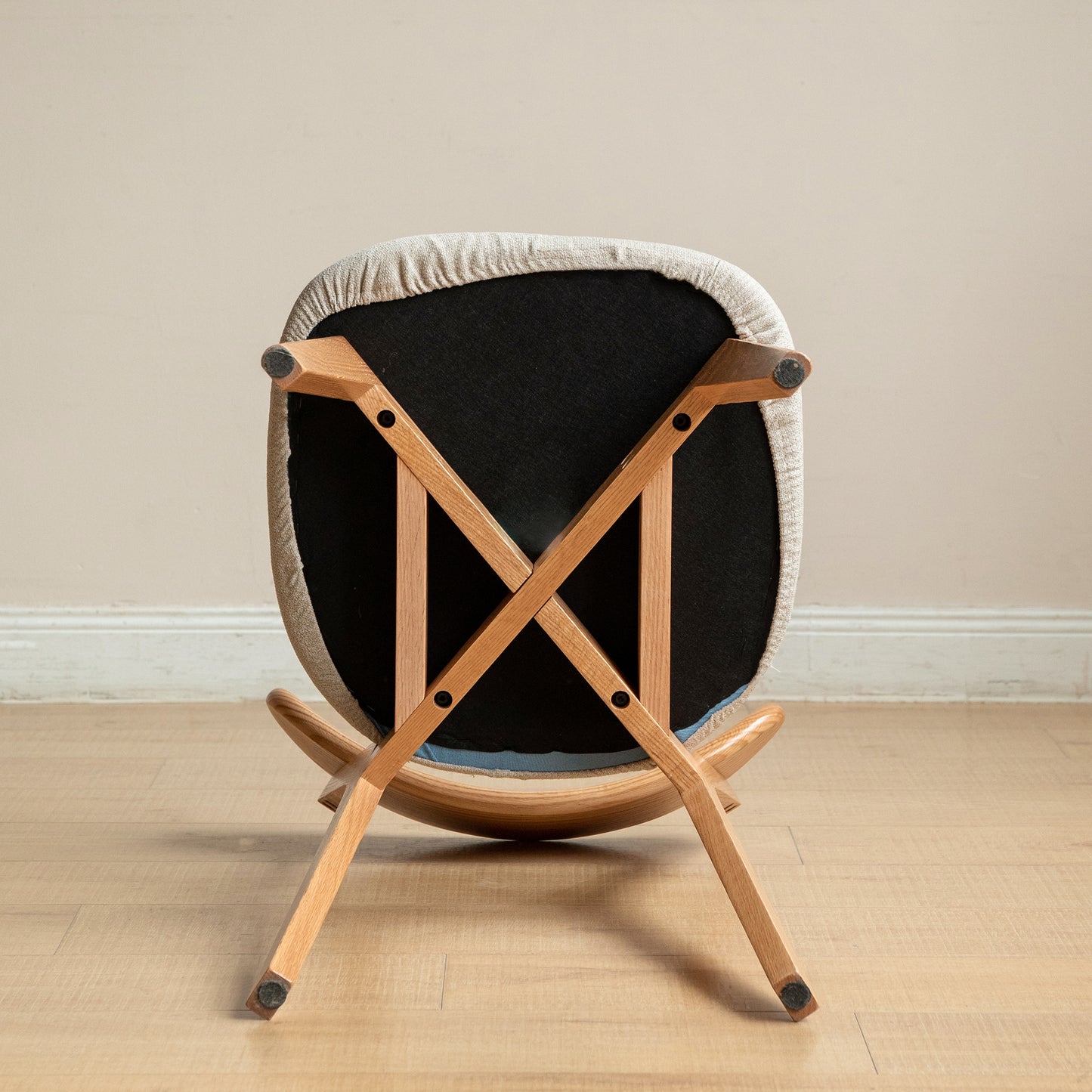 Underside view of a grey upholstered rocking chair with light wood legs