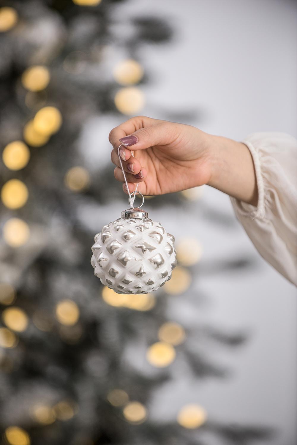 White and silver textured pinecone Christmas ornament held by hand