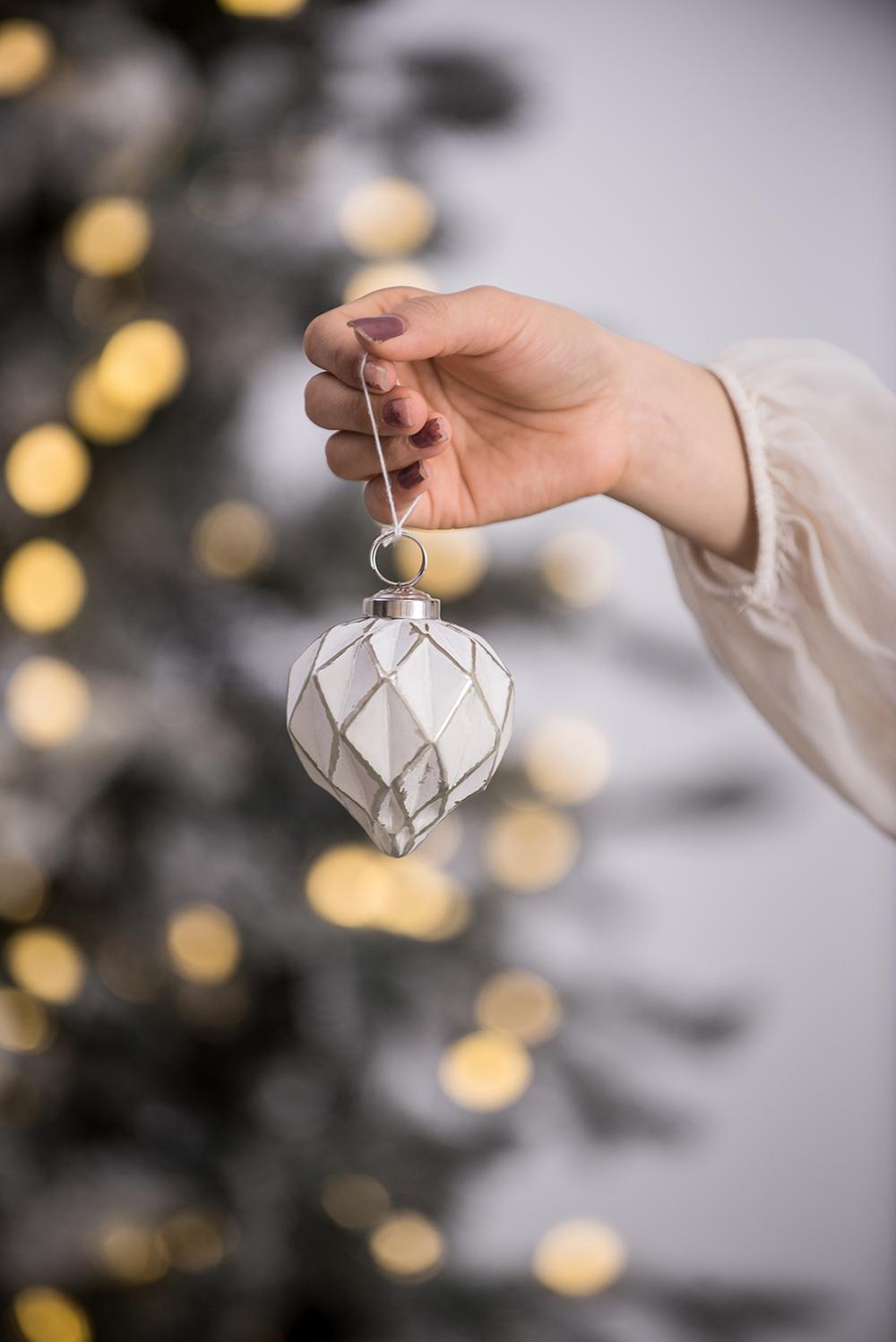 White diamond pattern Christmas ornament hanging from a hand