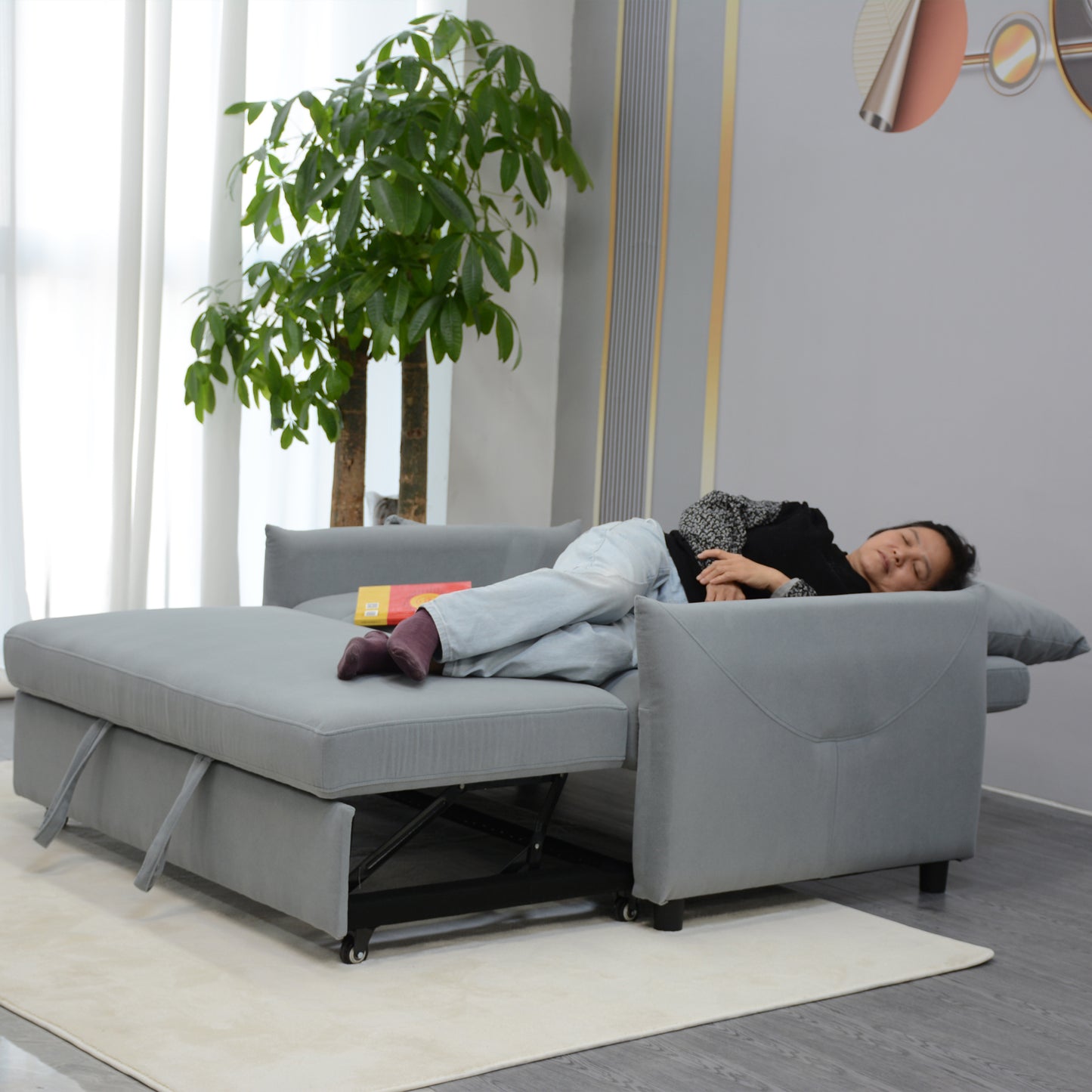 Gray upholstered pullout sofa bed with plush cushions and a sleeping person