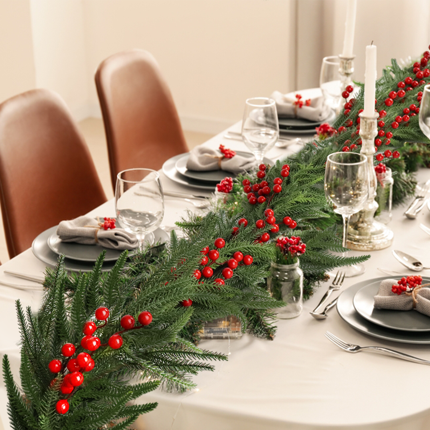Green artificial Christmas garland with red berries draped across a dining table setting