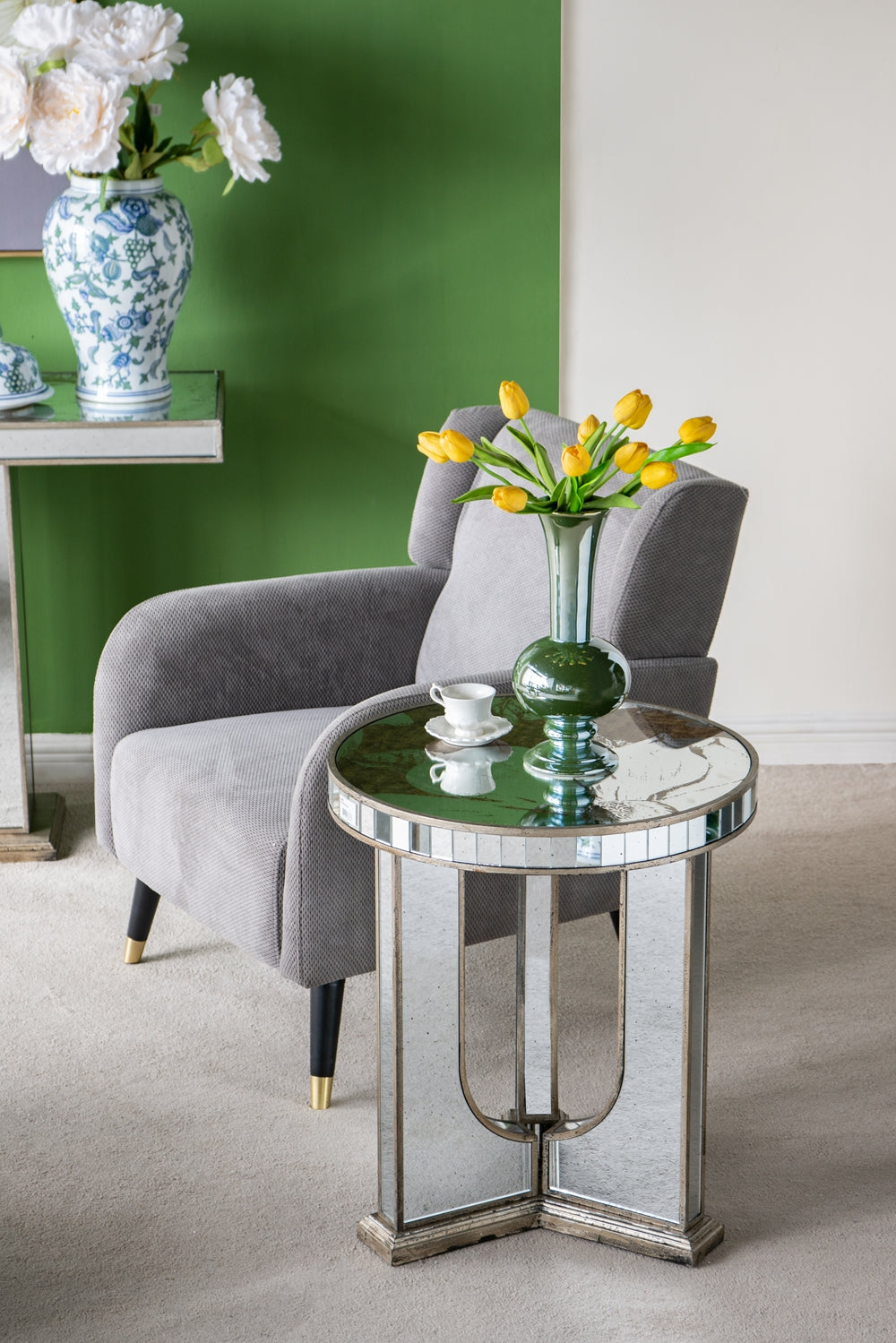 Gray textured armchair with goldcapped black legs next to a mirrored side table