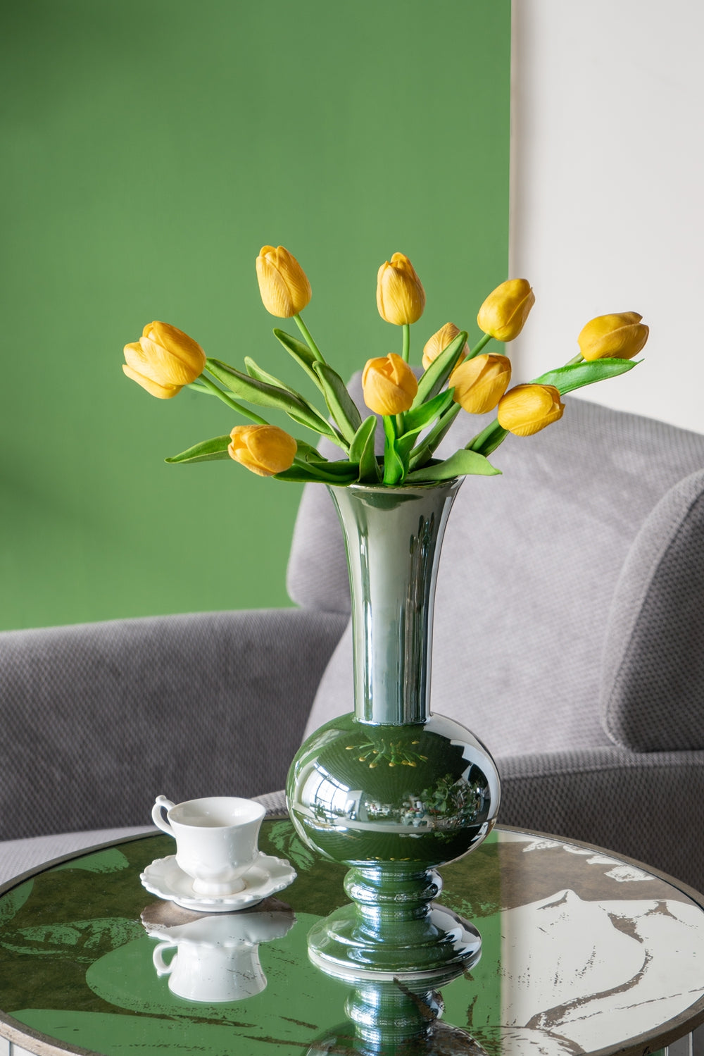 A bouquet of yellow artificial tulips arranged in a tall emerald green glass vase