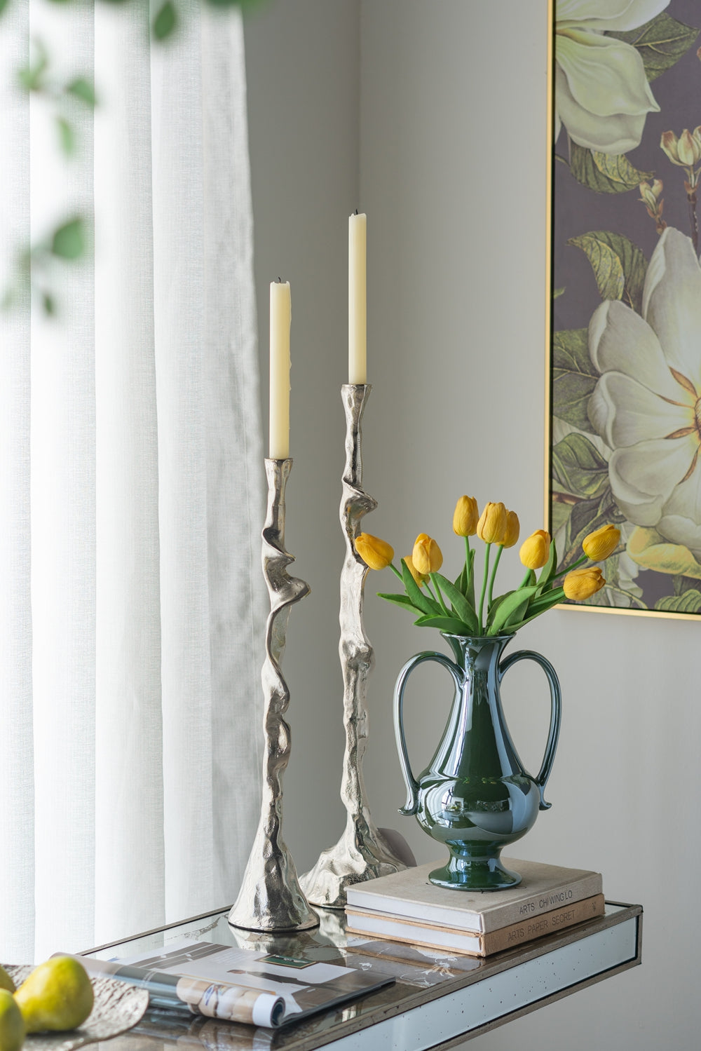 Tall silver abstract design candleholders with cream candles on mirrored table