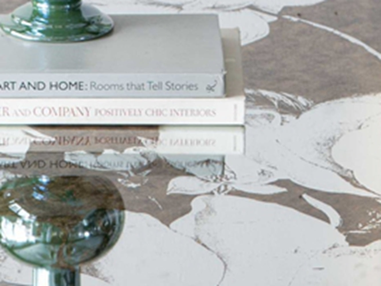 Stack of interior design books one titled ART AND HOME Rooms that Tell Stories on a floral patterned surface