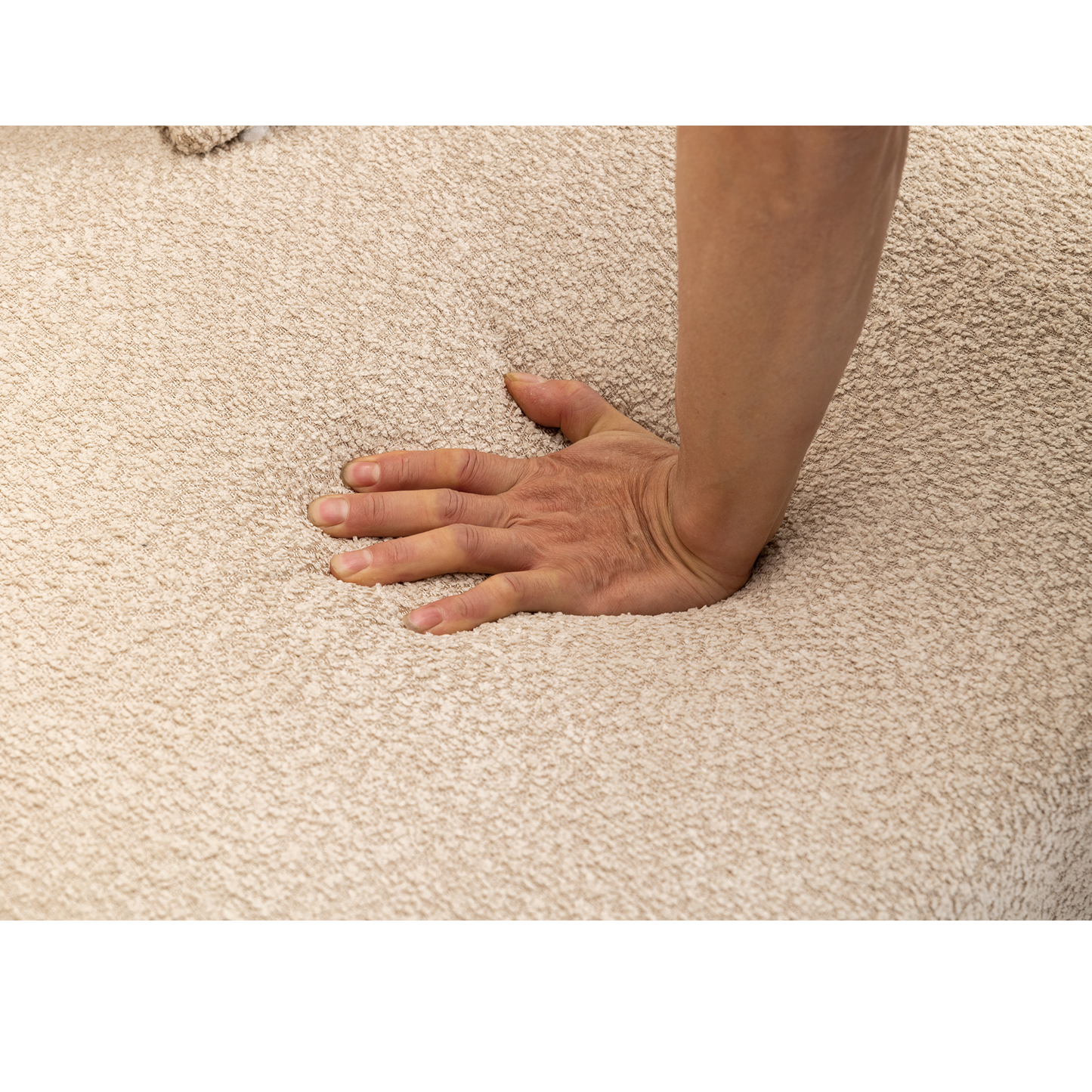 Closeup of a hand pressing into a soft beige textured fabric showcasing plushness