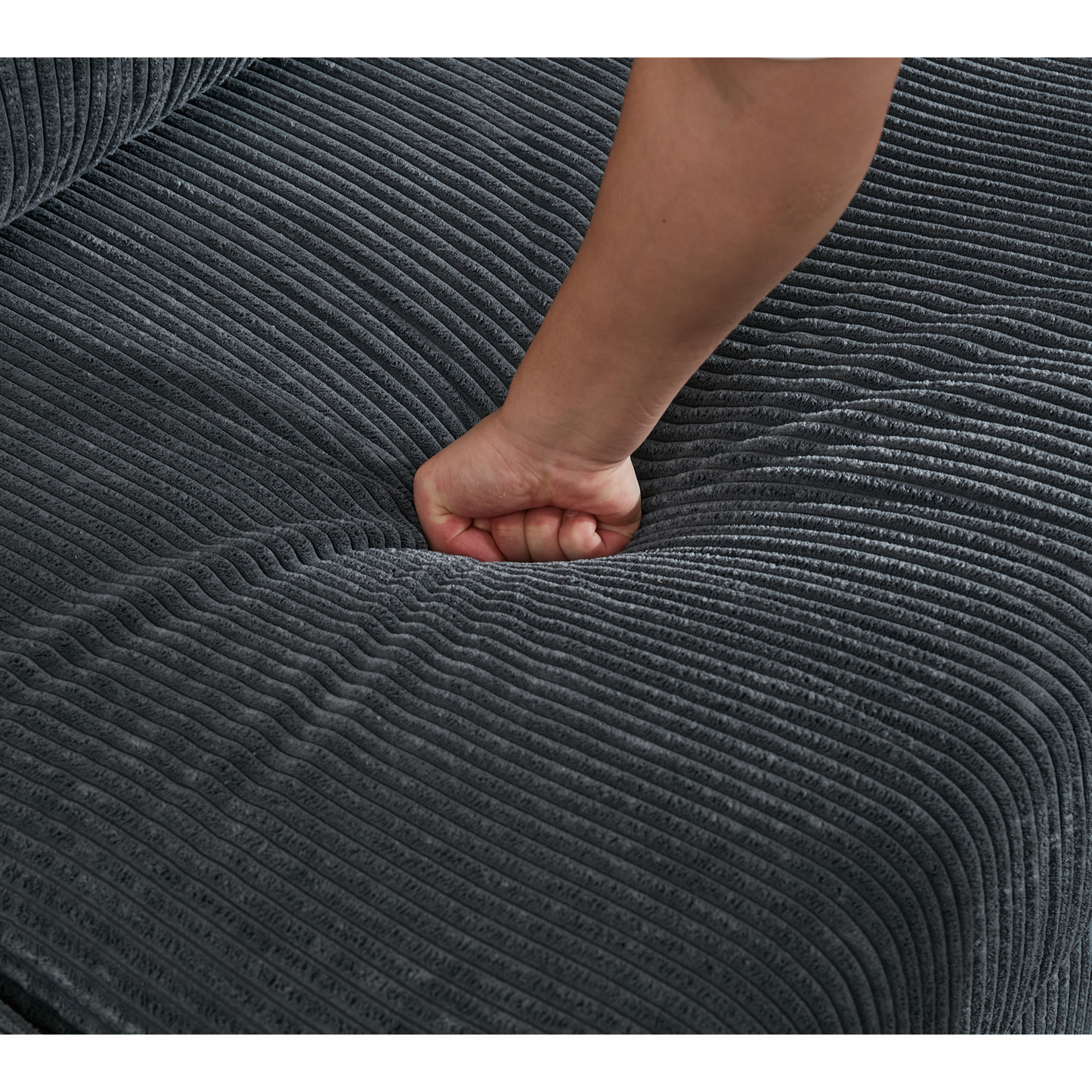 Closeup of a hand pressing into plush charcoal corduroy fabric highlighting sofa softness