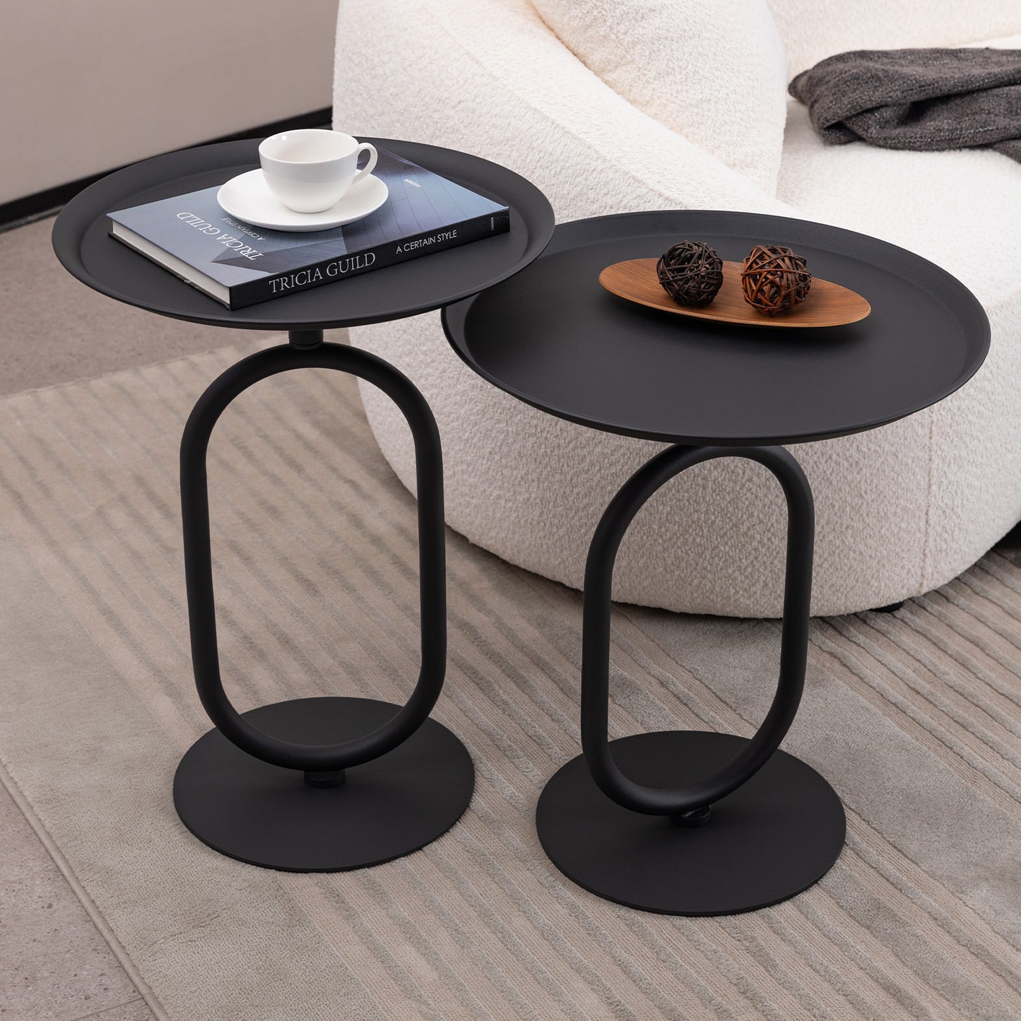 Black metal side table with oval base holding a book and coffee cup