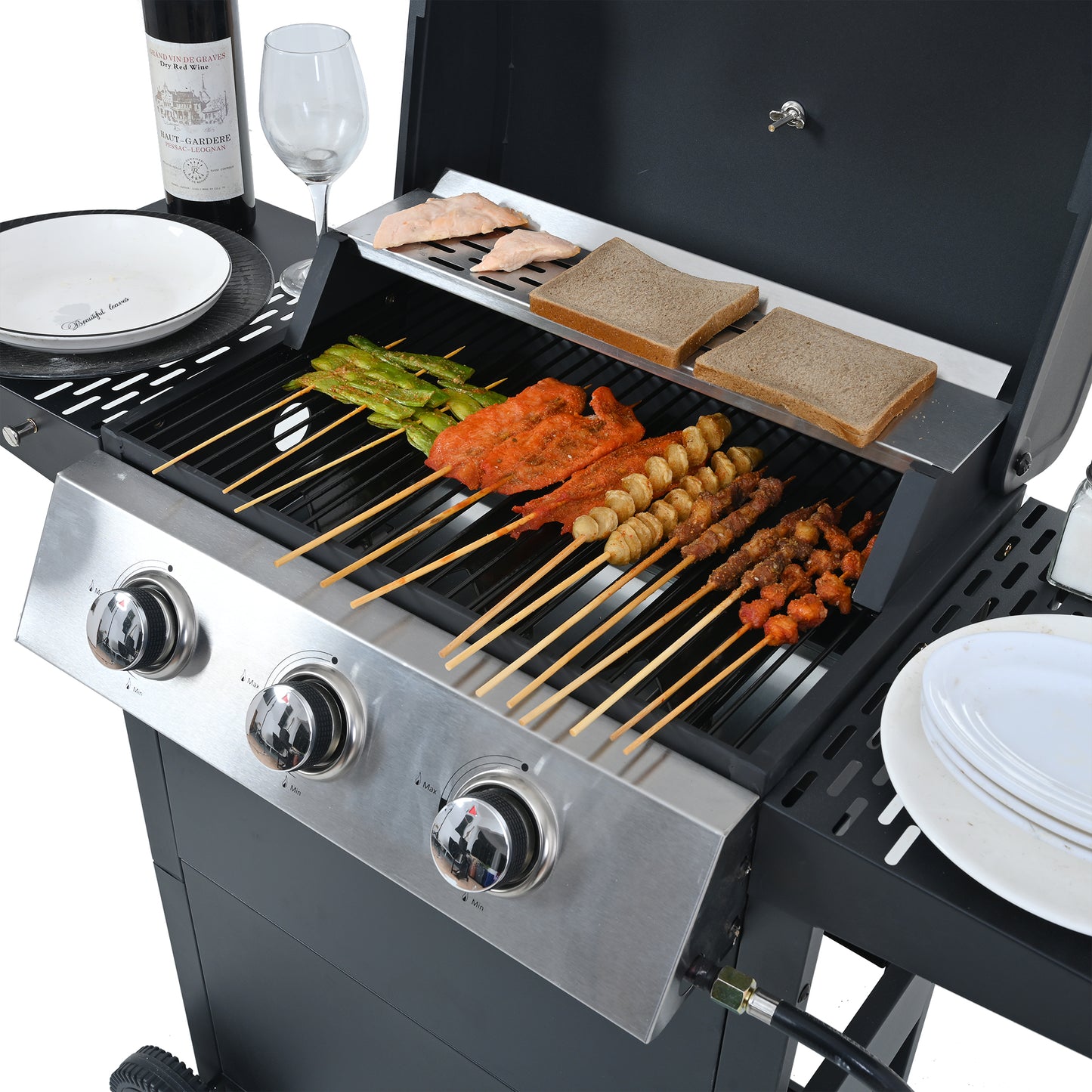 Stainless steel gas grill with skewers of chicken meatballs and vegetables cooking on grates