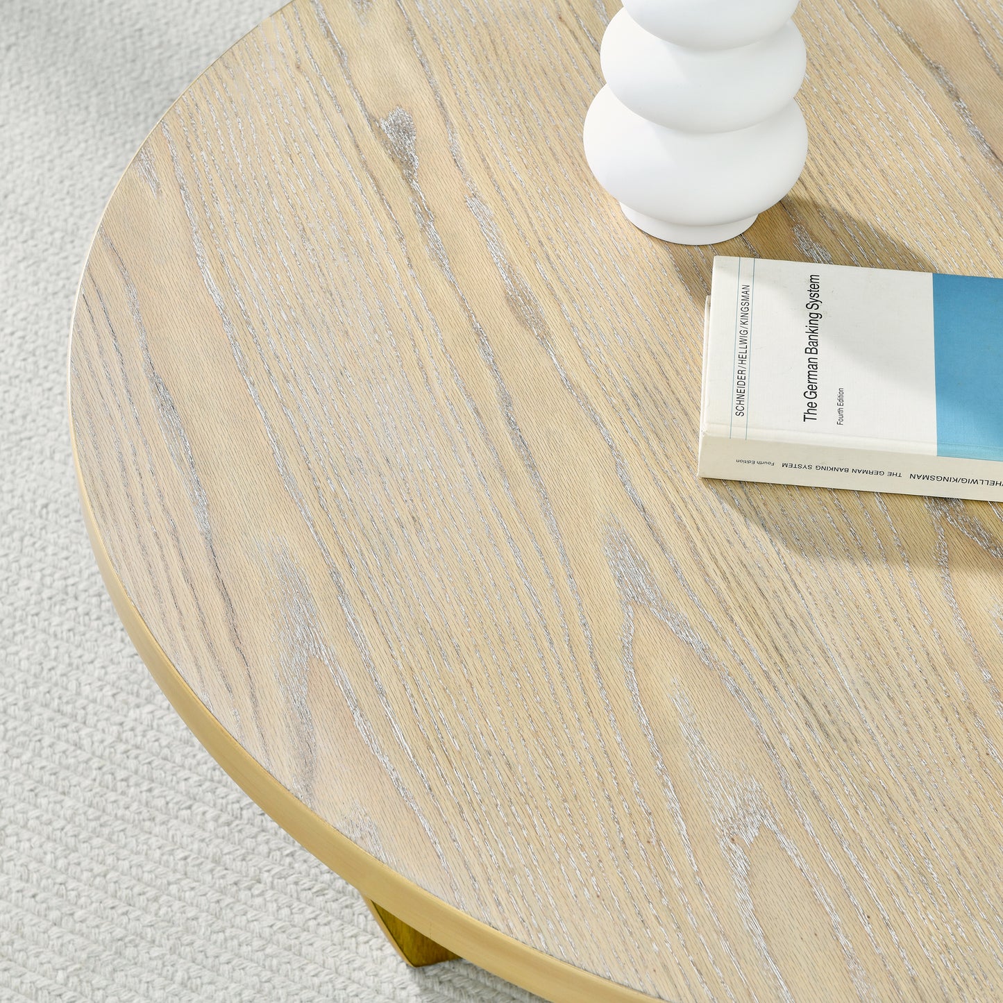 Round ash wood coffee table with brushed brass rim and textured rug