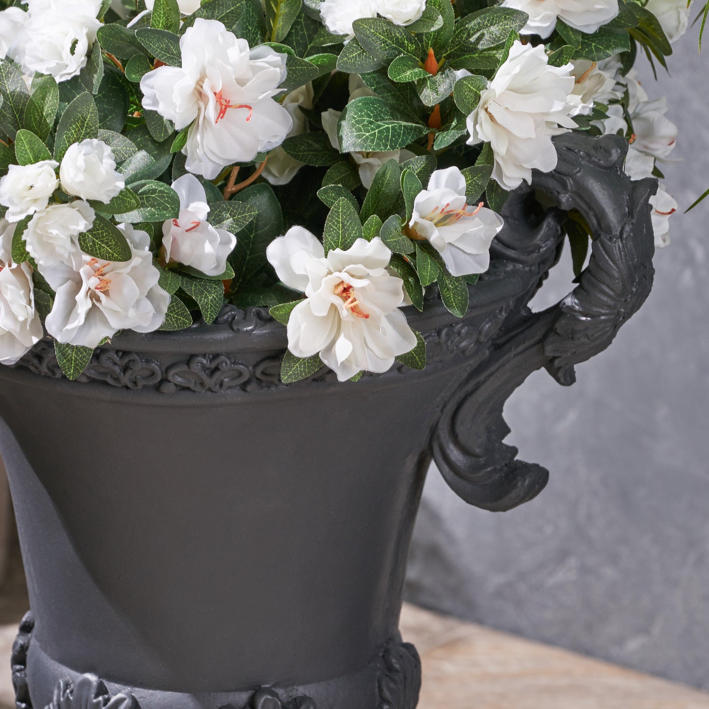 Closeup of a decorative black urn overflowing with lush white azalea flowers and green foliage