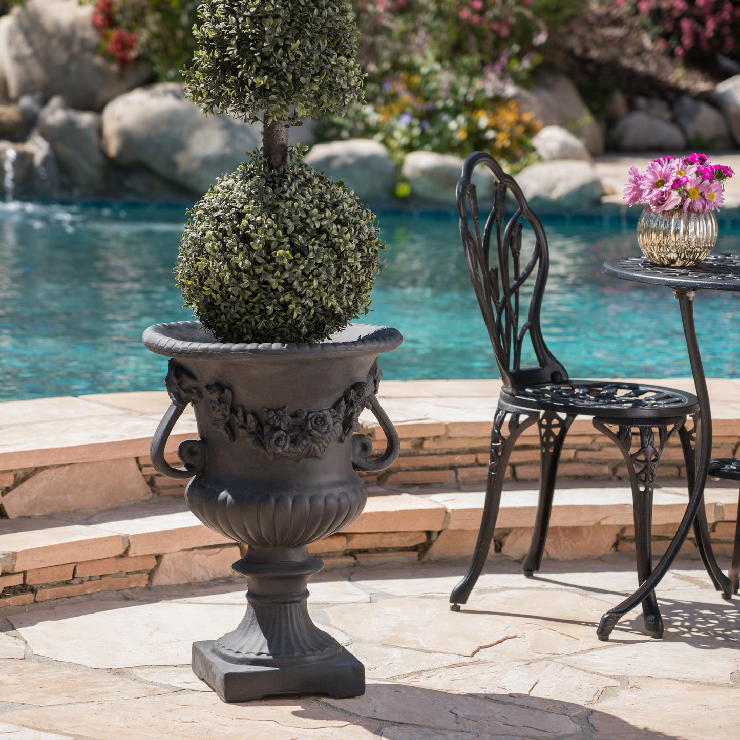 Dark grey cast iron urn planter with floral relief holding a sculpted boxwood topiary